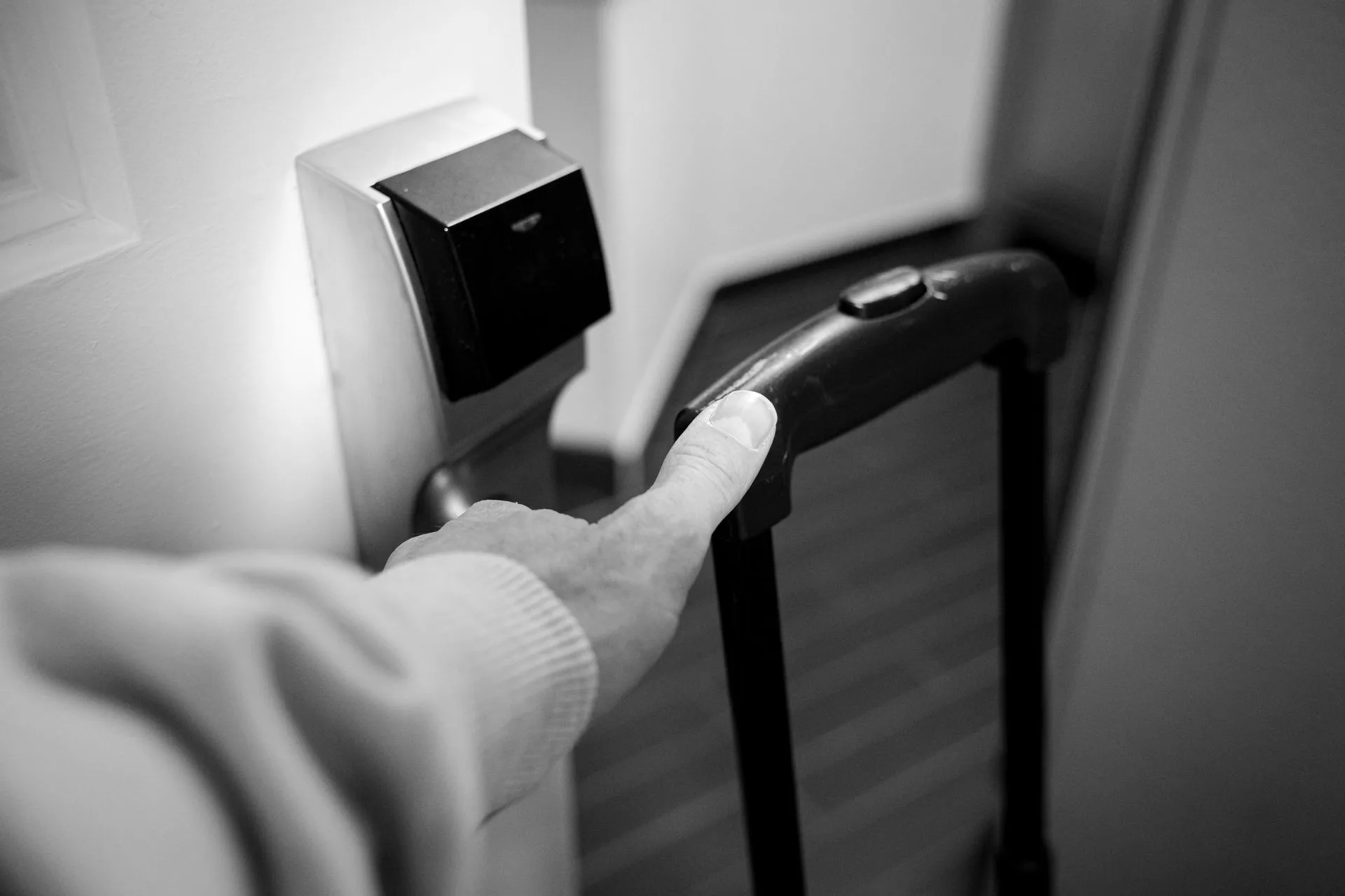 A monochrome photograph of a hand opening a hotel room door with a luggage handle, illustrating 1Password CTO says AI agent access should be scoped to one task at a time