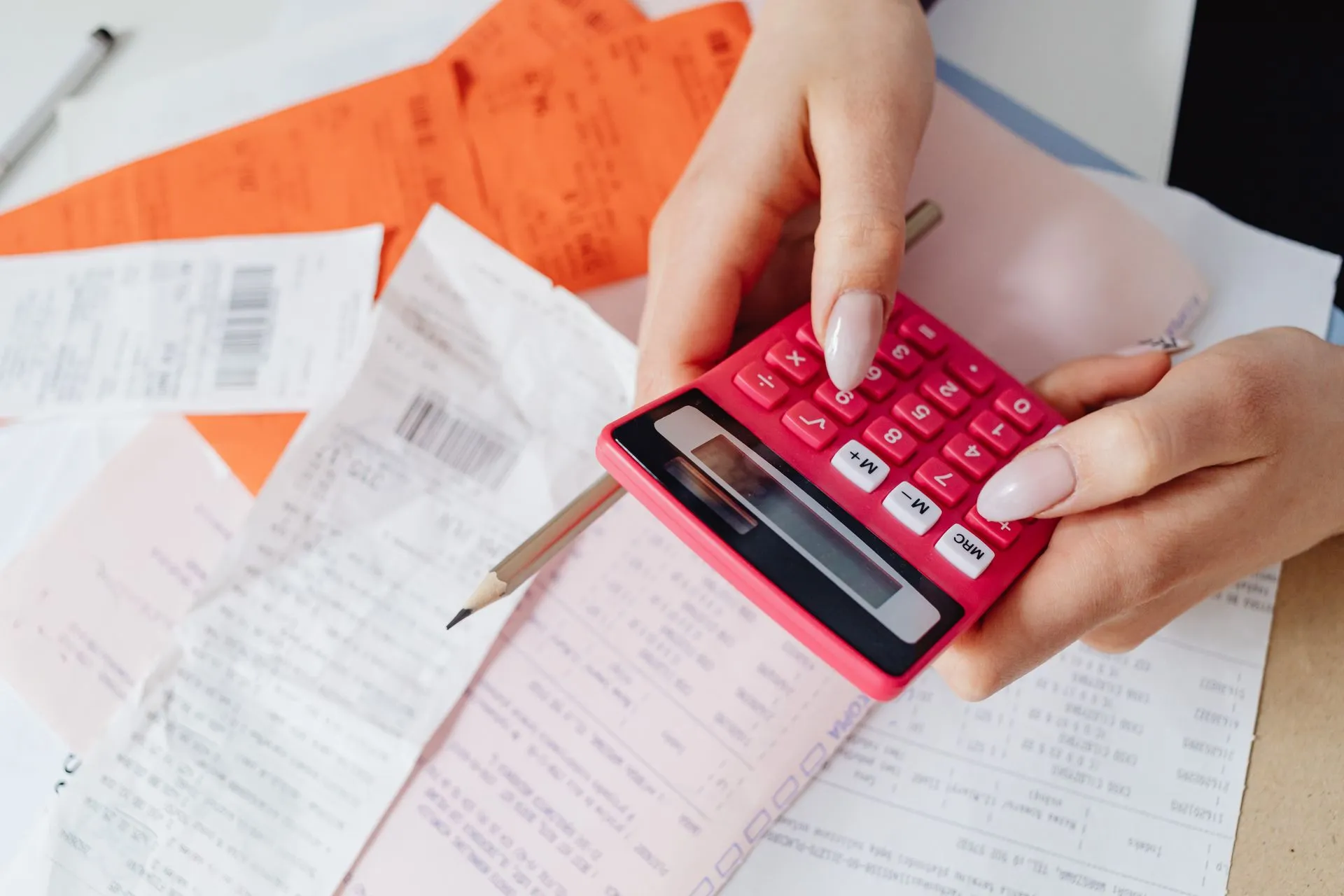 Hands using a pink calculator to manage expenses amidst various receipts and documents, illustrating Salesforce and Adobe show AI credits pricing is making SaaS bills variable