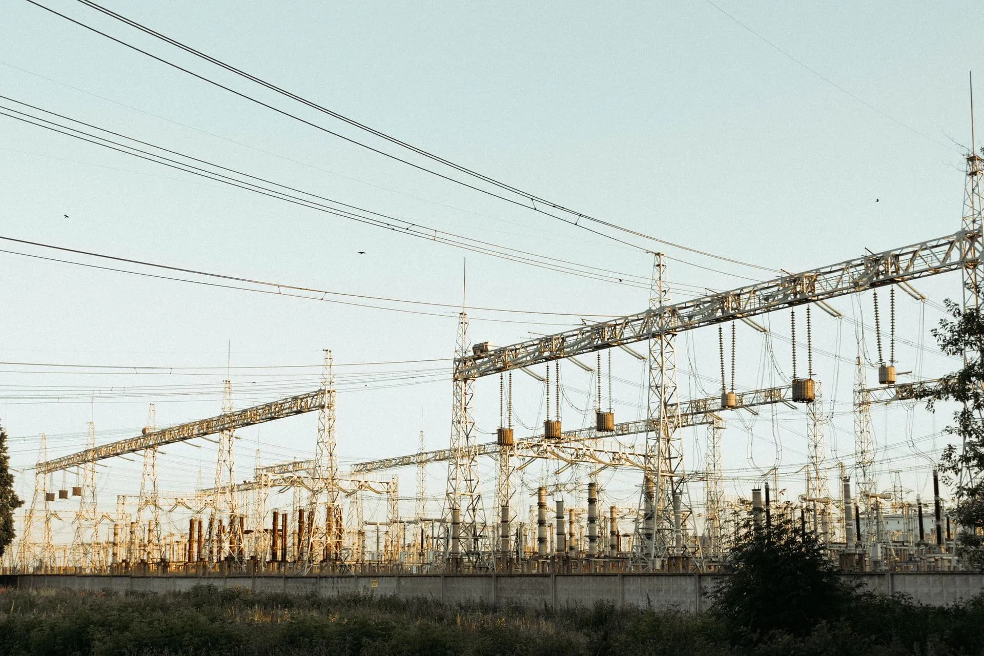 A wide view of an industrial electrical substation with power lines and towers outdoors, illustrating House and Massachusetts move to shift AI data center power costs onto builders