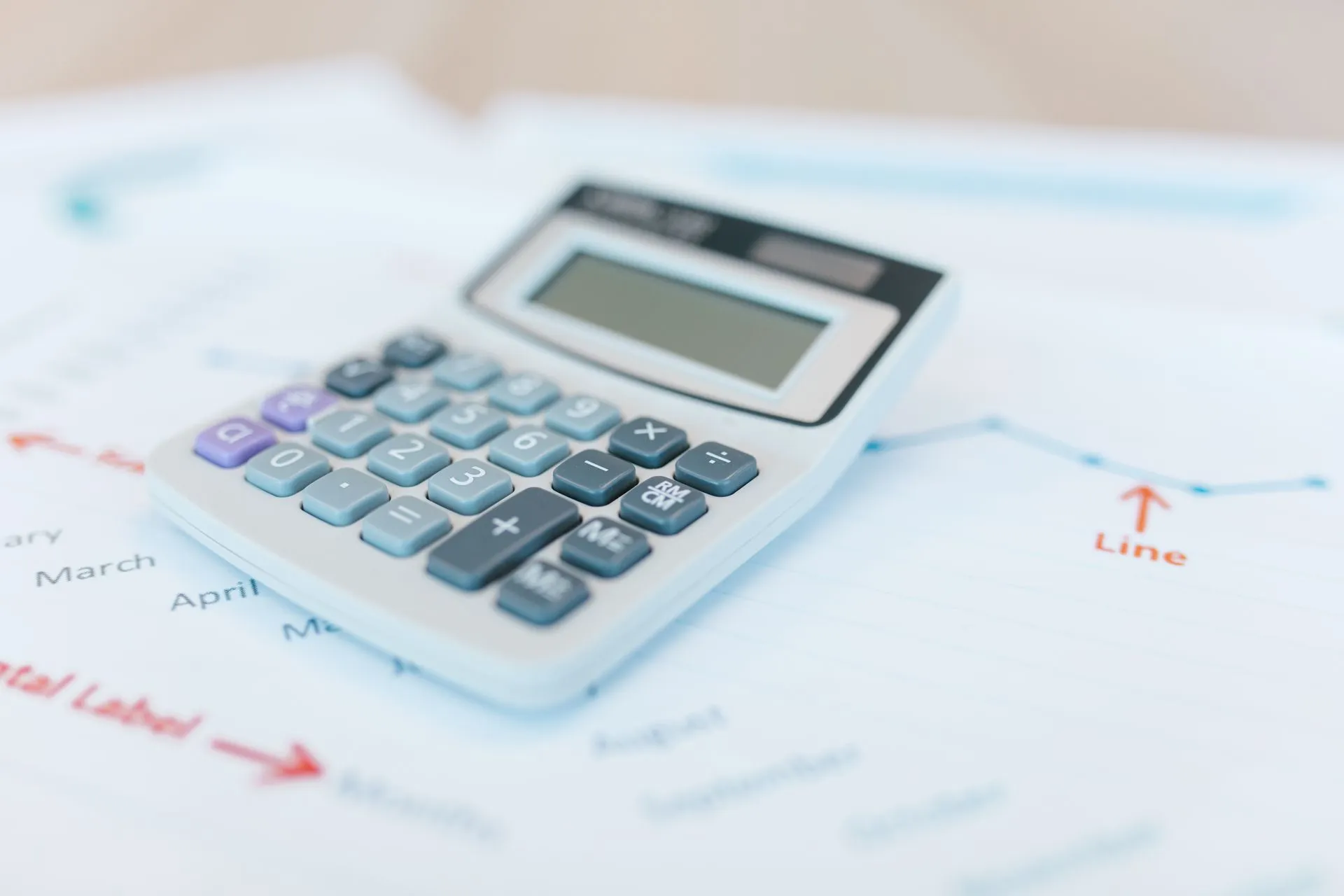 Close-up of a calculator on financial documents with graphs and analysis papers, illustrating AI model pricing splits as OpenAI and Anthropic cut rates while DeepSeek has raised its own