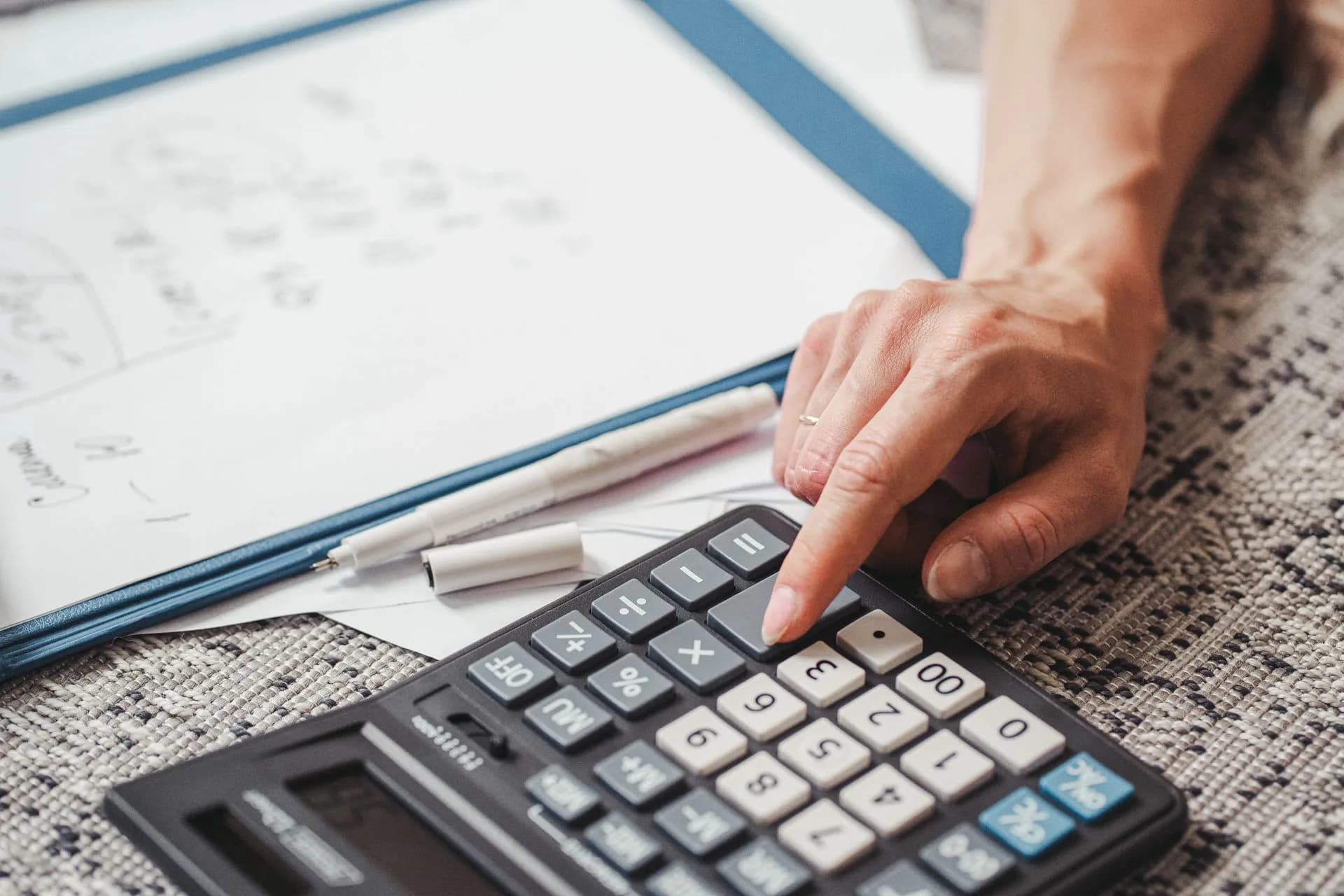A hand using a calculator on top of documents, indicating financial calculation or analysis, illustrating AI usage-based pricing spreads