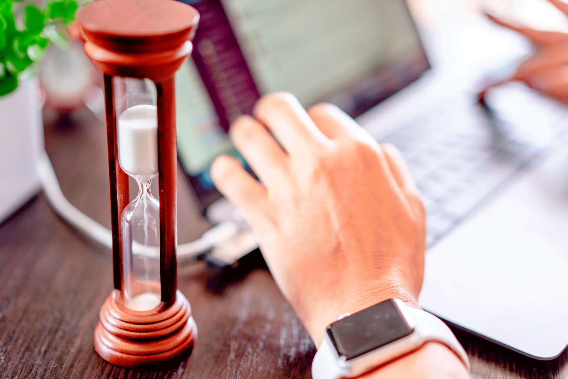 Close-up of a hand on a laptop with an hourglass, symbolizing time management and productivity, illustrating AI usage limits spread as OpenAI, Apple and Meta add caps, waitlists and