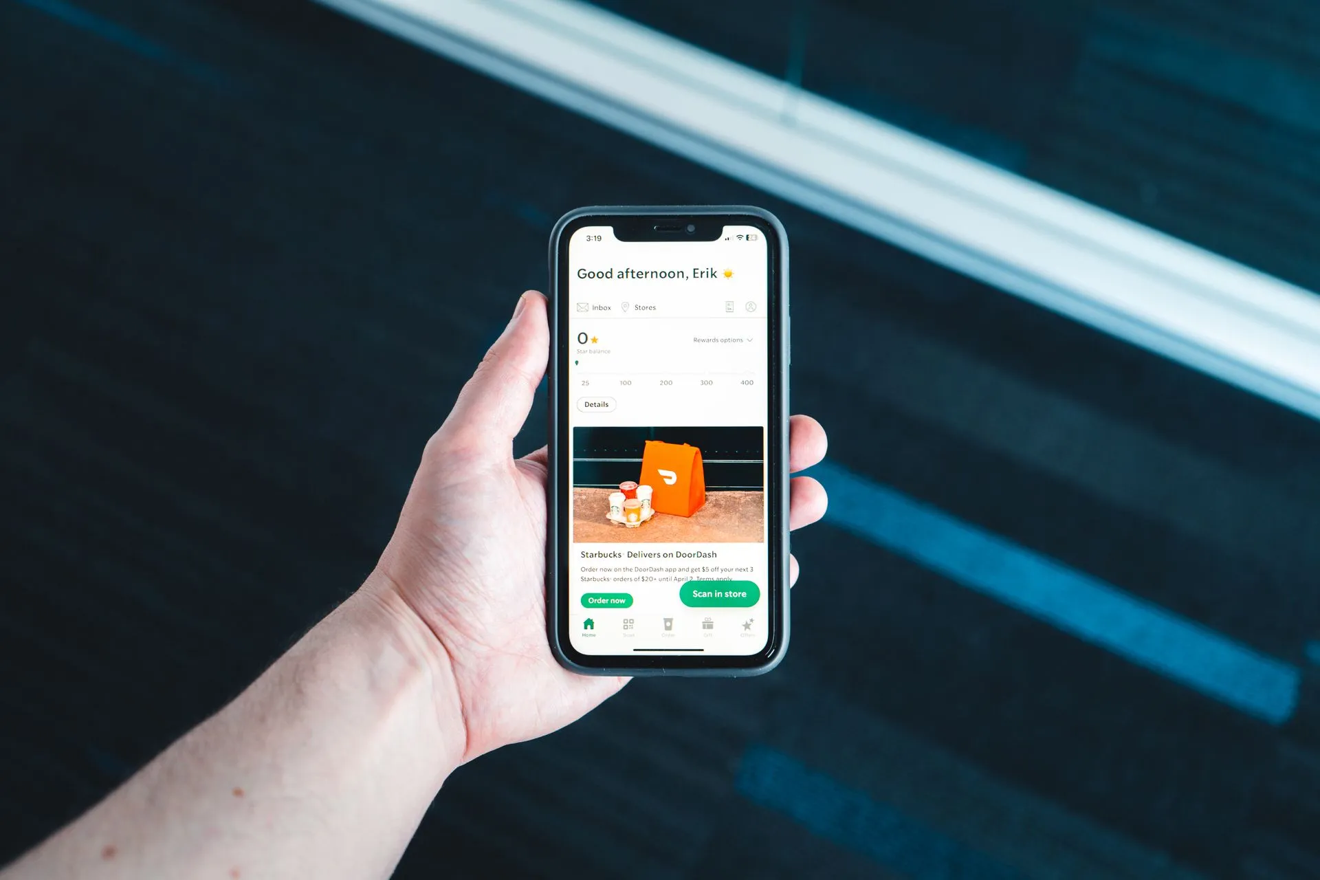 Hand holding smartphone with food delivery app on screen in bright setting, illustrating Airbnb AI search, DoorDash's text-to-order agent and Instagram's Edits assistant