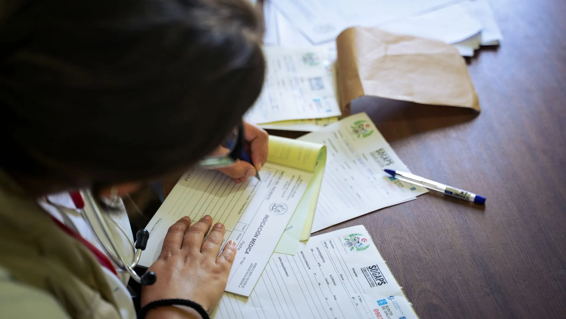 A doctor fills out medical forms indoors, focusing on patient care and documentation, illustrating Alight Abett acquisition adds a data engine that links employers' benefits vendors