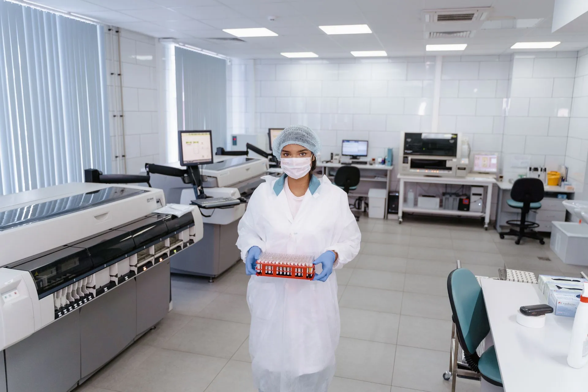 A scientist in protective gear holding test samples in a modern laboratory setting.
