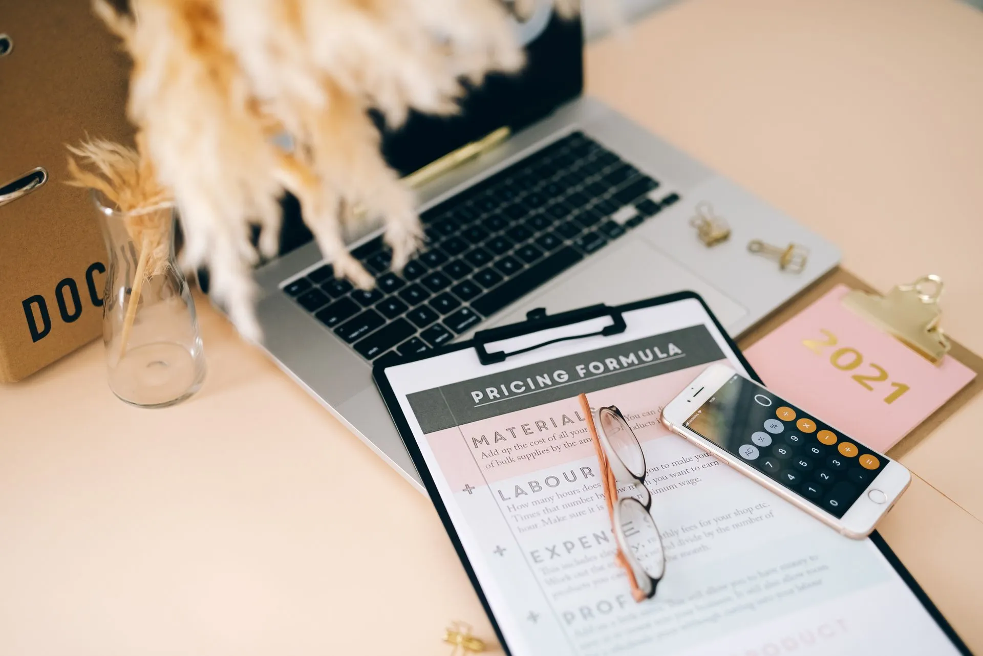 Organized office desk with pricing formula document, laptop, and smartphone calculator, illustrating Anthropic Claude Haiku 5.5 launches at $0.10 per million input tokens, Sonnet cache