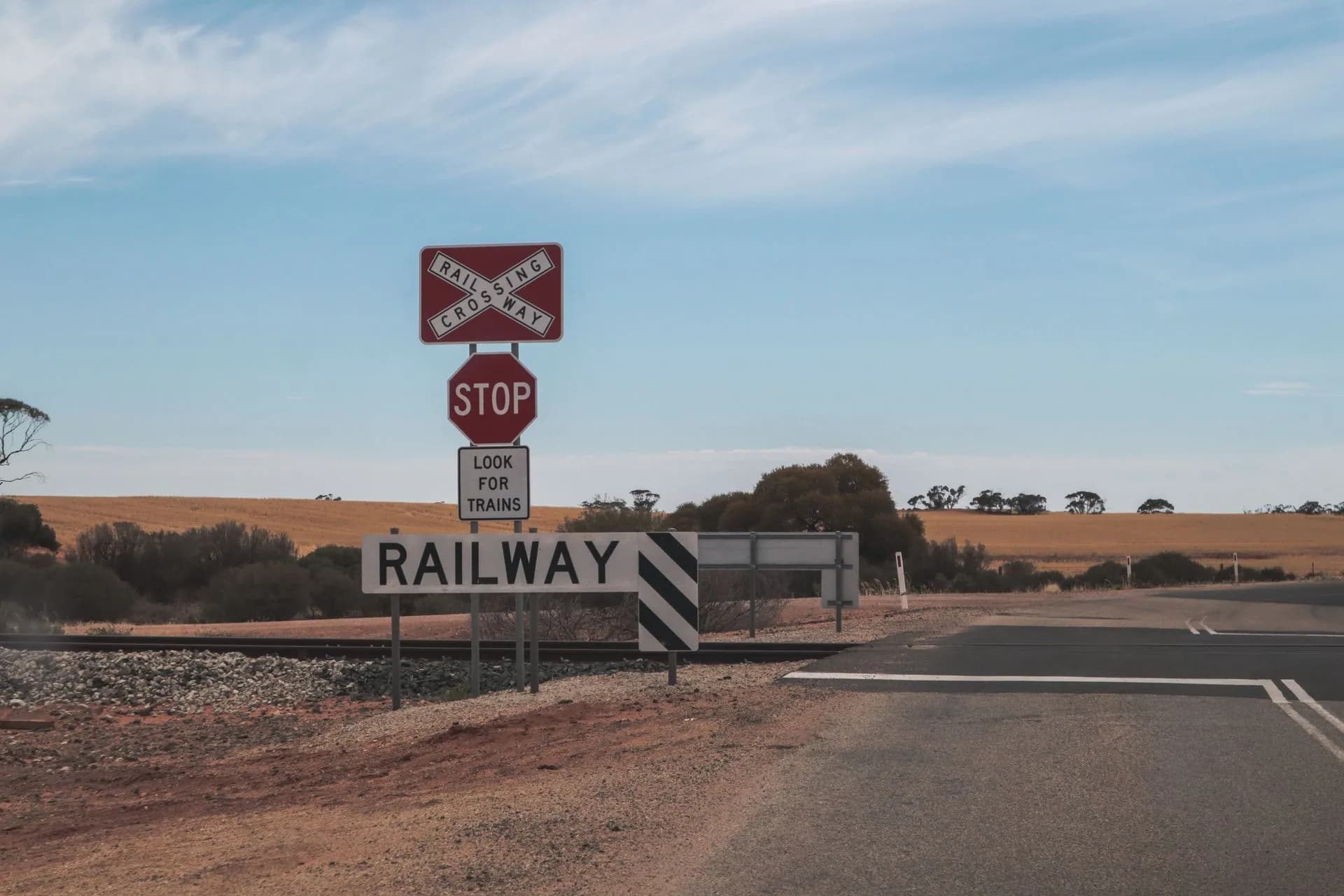 Railway crossing in a rural desert setting with clear skies and open road, illustrating Anthropic Queensland data center deal puts Claude in a proposed A$32 billion AI campus