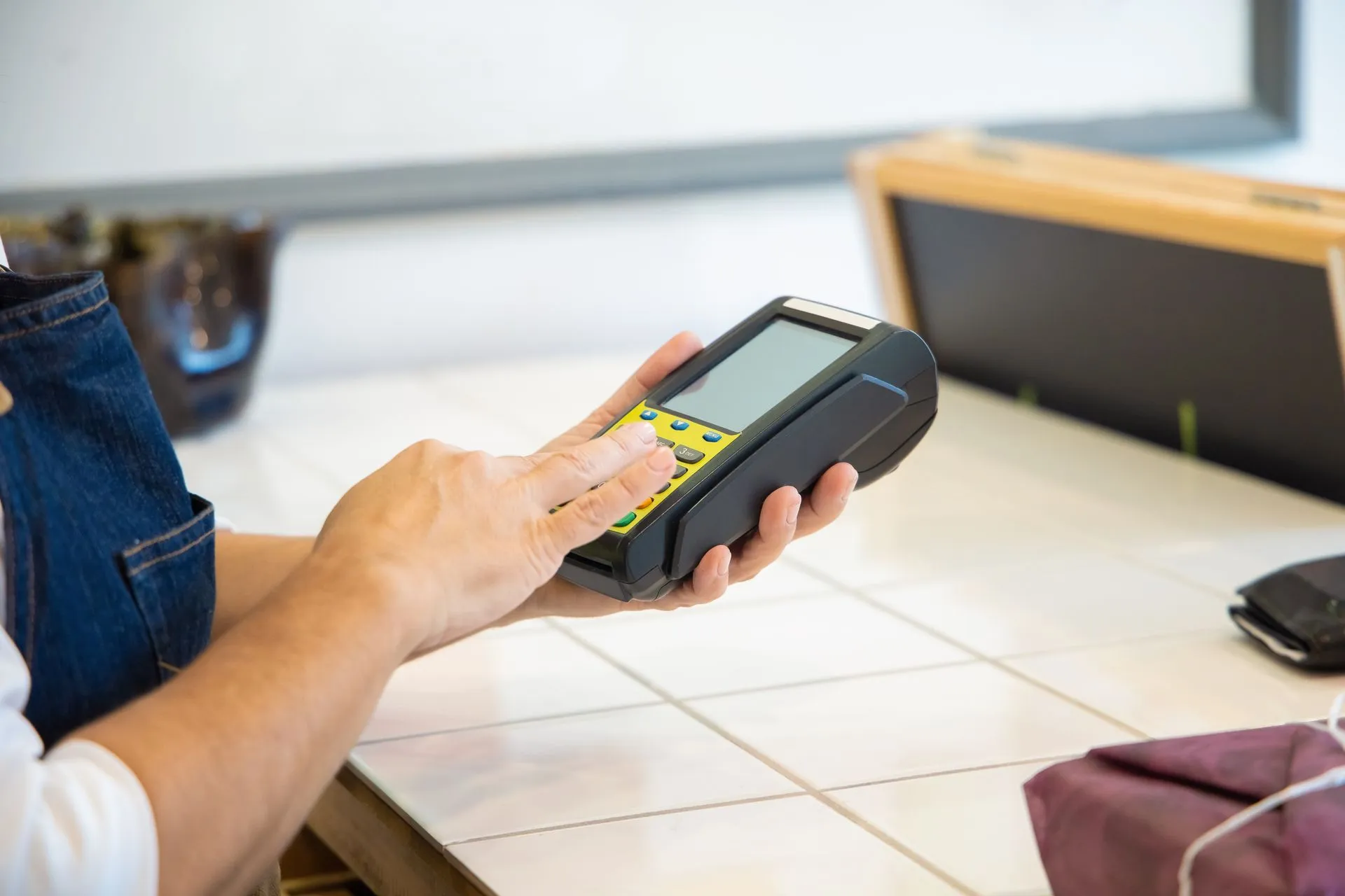 Close-up of hands using a POS machine in a retail setting, emphasizing digital payment, illustrating Apple Pay in India launches with Axis Bank only