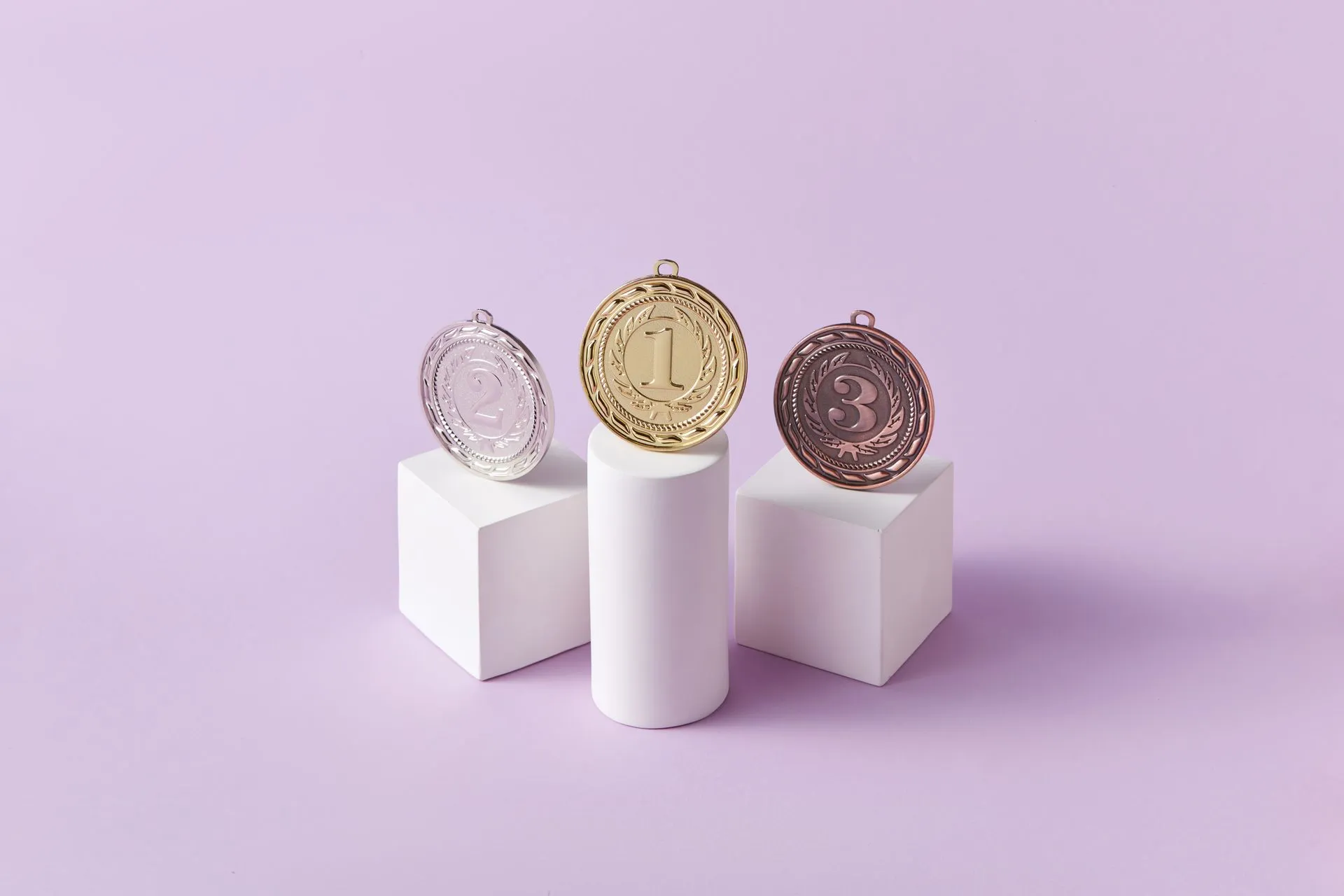 Gold, silver, and bronze medals displayed on white pedestals with a pink background, illustrating AI leaderboard Arena raises $200M at $3.1B valuation, nearly doubling in 10 months