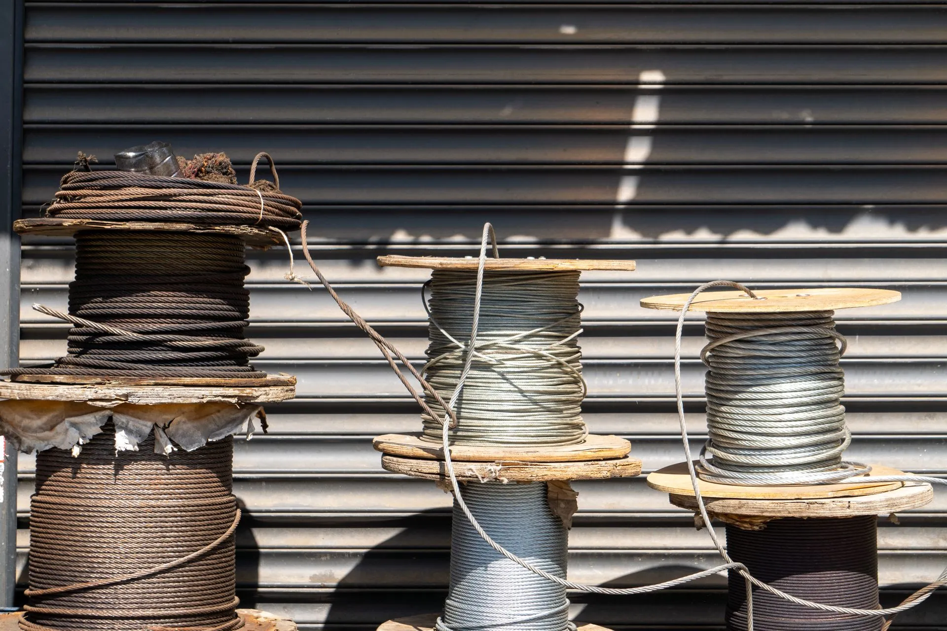 Multiple large spools of industrial cable placed outdoors in front of a closed shutter, illustrating AT&T Corning fiber deal tops $3 billion as carriers lock in supply for AI-era demand