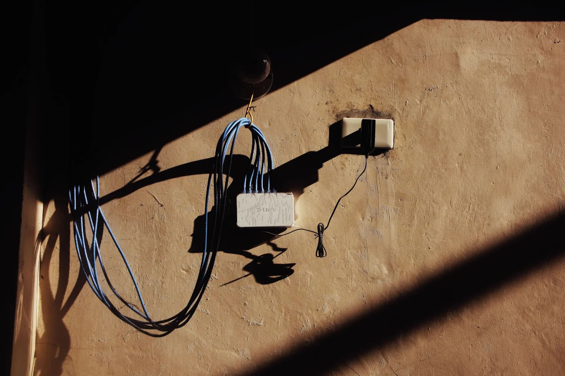 Electric blue wires connected to network adapter plugged in socket on shabby brown wall of building on street with shadow, illustrating AWS and Cloudflare decision models push cheaper routing