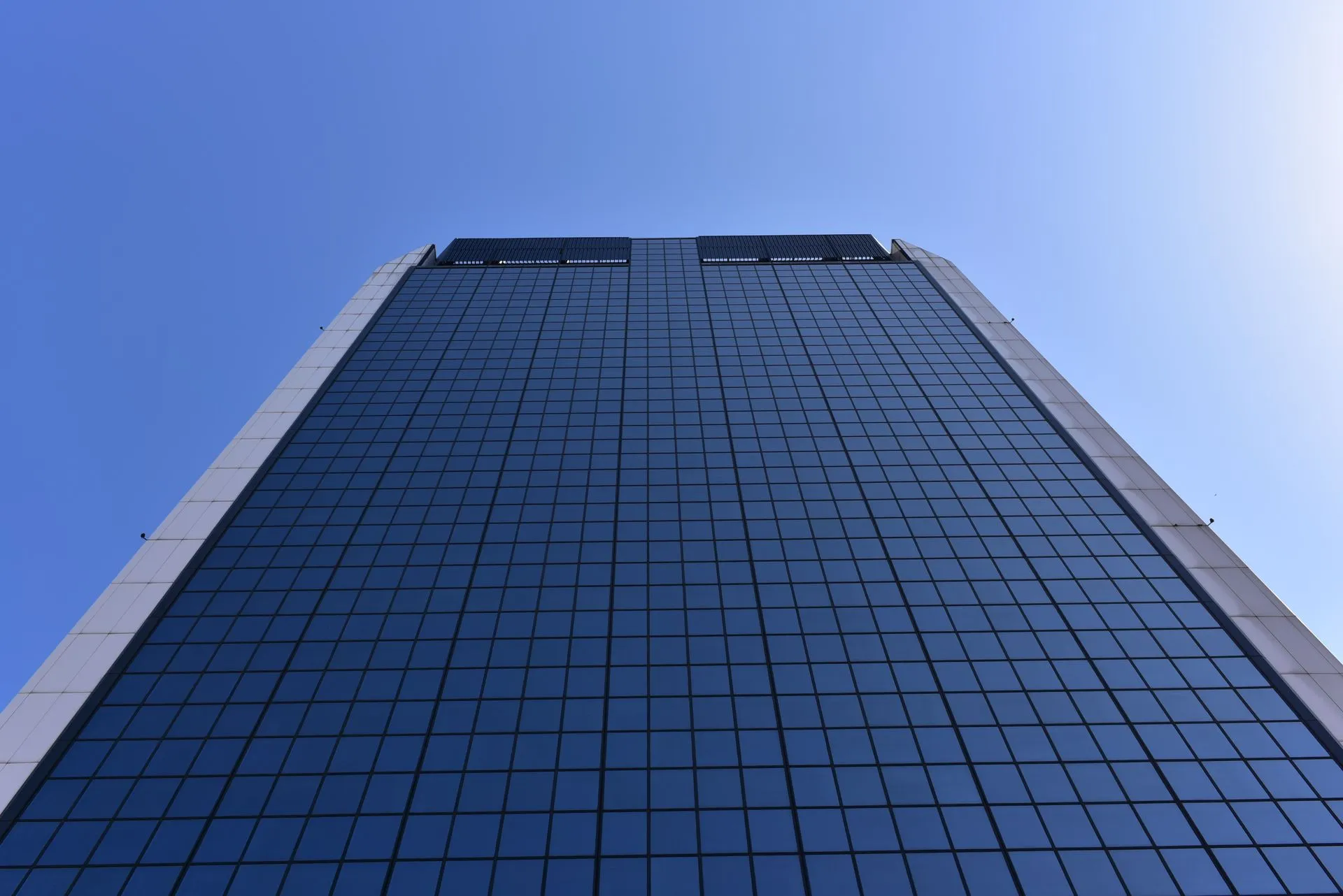 Low-angle shot of a tall glass skyscraper against a clear blue sky, showcasing modern architecture.