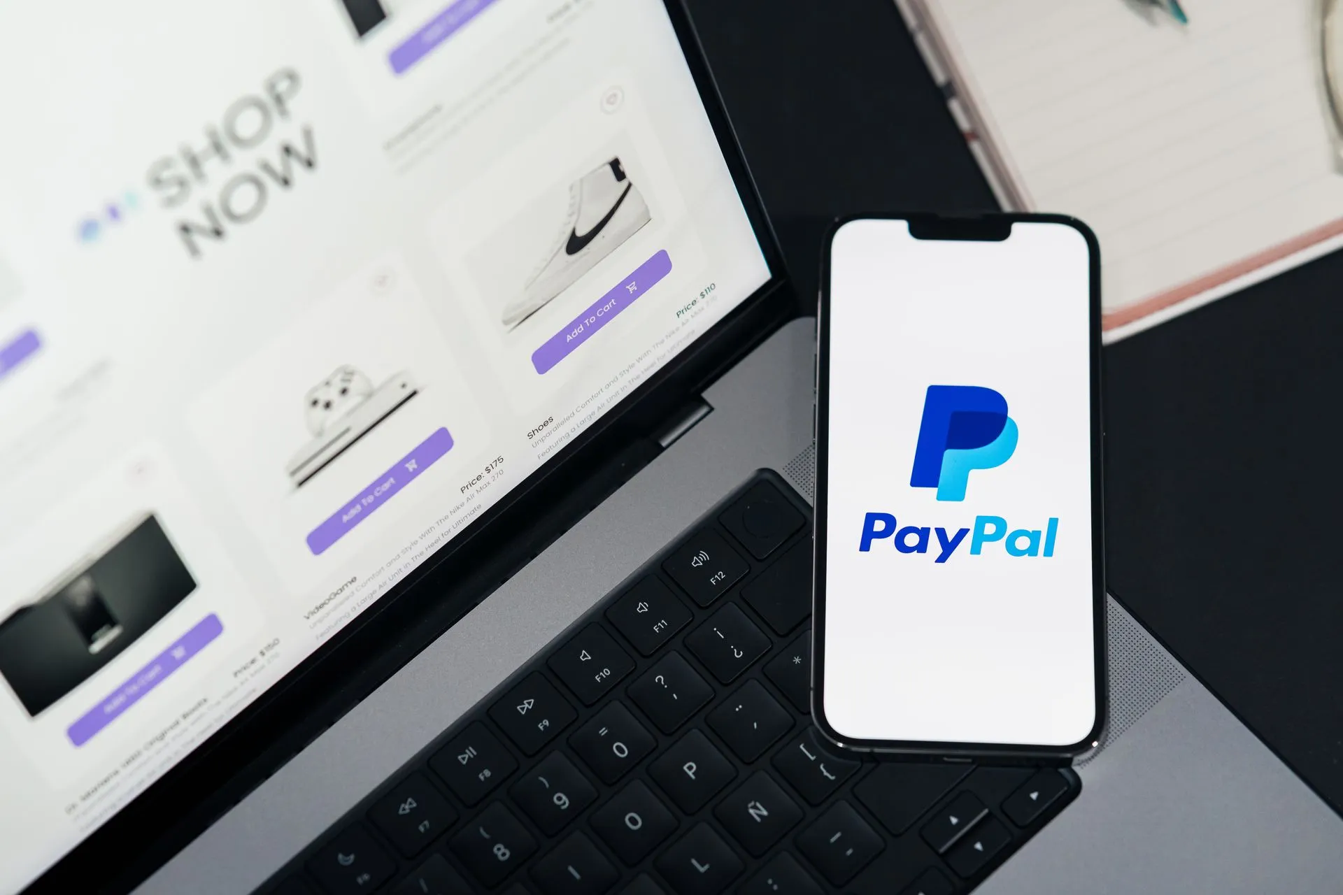Smartphone displaying PayPal logo next to laptop with online shopping site open, illustrating Cloudflare says bot traffic passed human traffic in May 2026 as Shopify lets AI agents buy