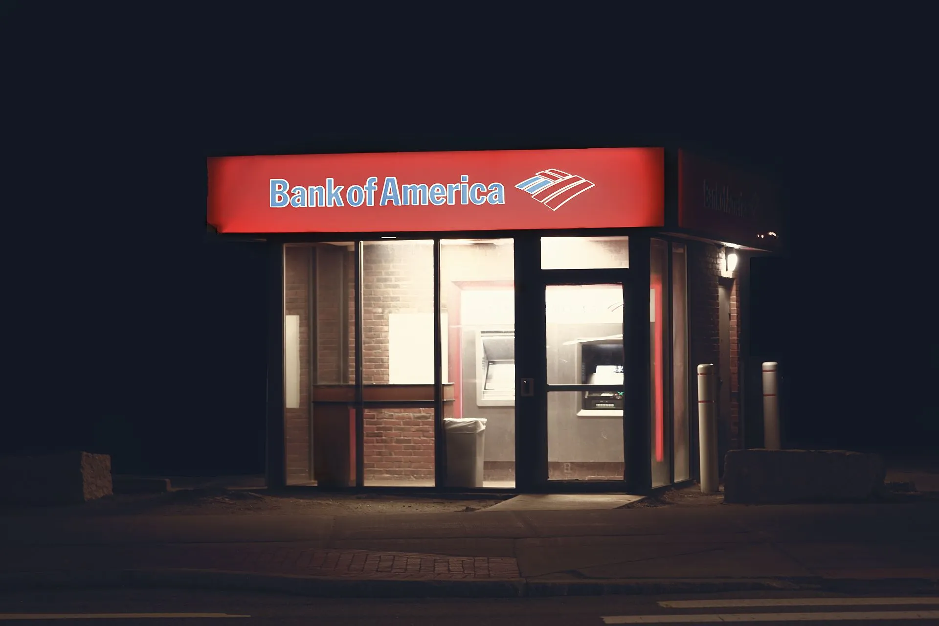 Illuminated Bank of America ATM structure against a dark nighttime backdrop in Boston, illustrating Brink's NCR Atleos deal faces UK in-depth probe threat