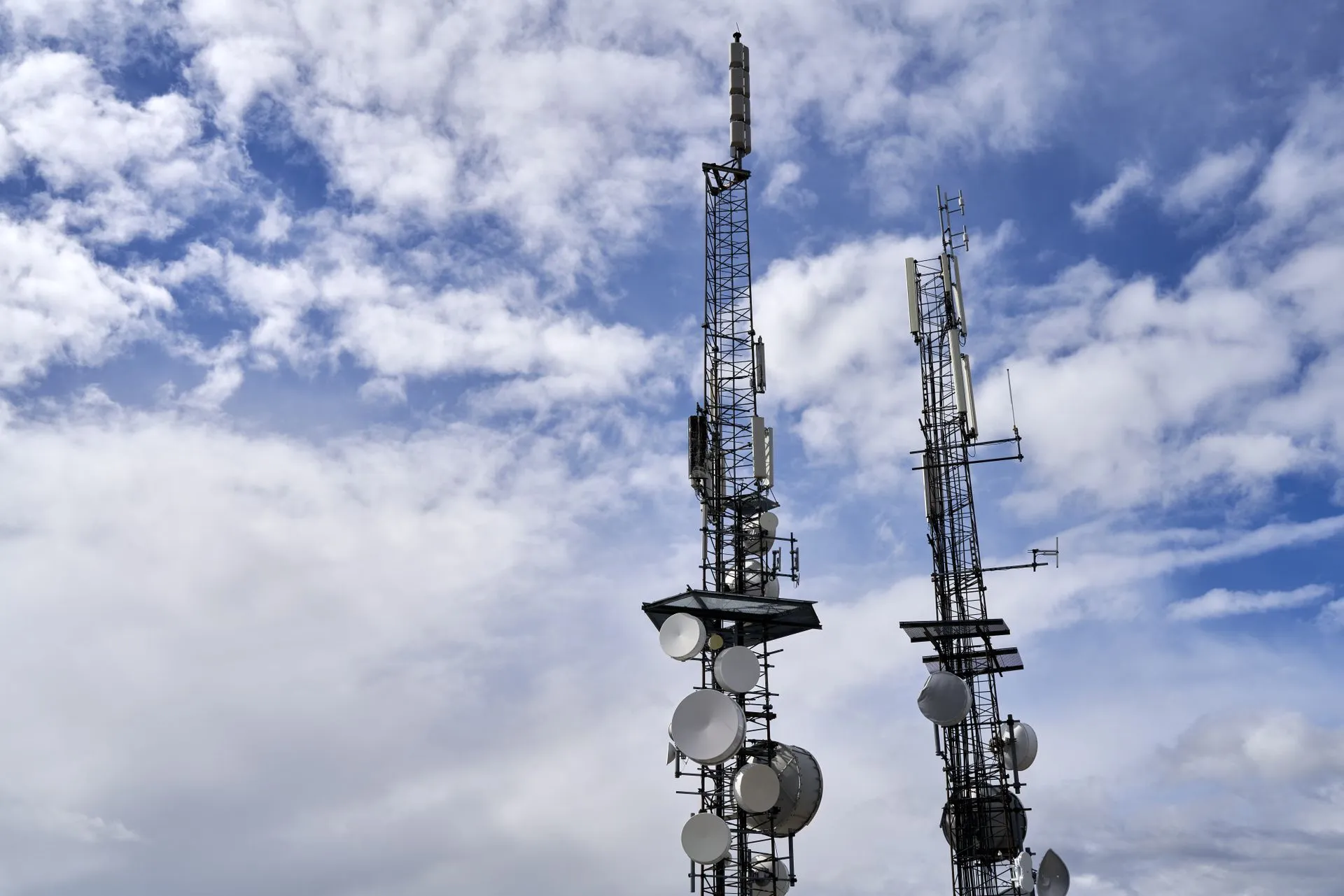 Telecommunication towers with antennas and dishes under a bright cloudy sky, illustrating Cameron Wagenius sentenced to 70 months for hacking and extorting telecom companies