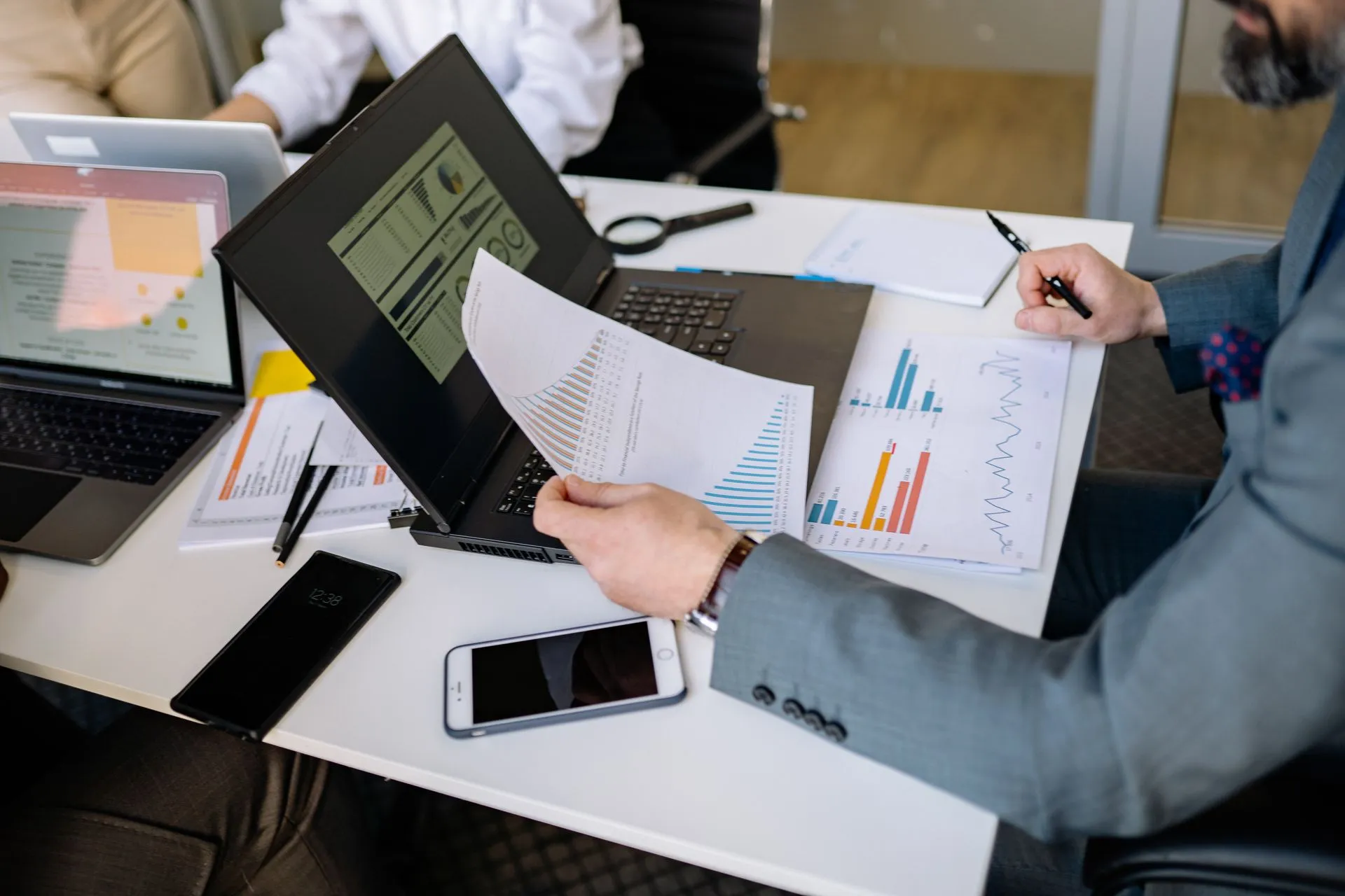 Professionals analyzing charts and graphs on laptops during a business meeting, illustrating OpenAI launches ChatGPT Space and Pages, moving onto partner Microsoft's Office turf