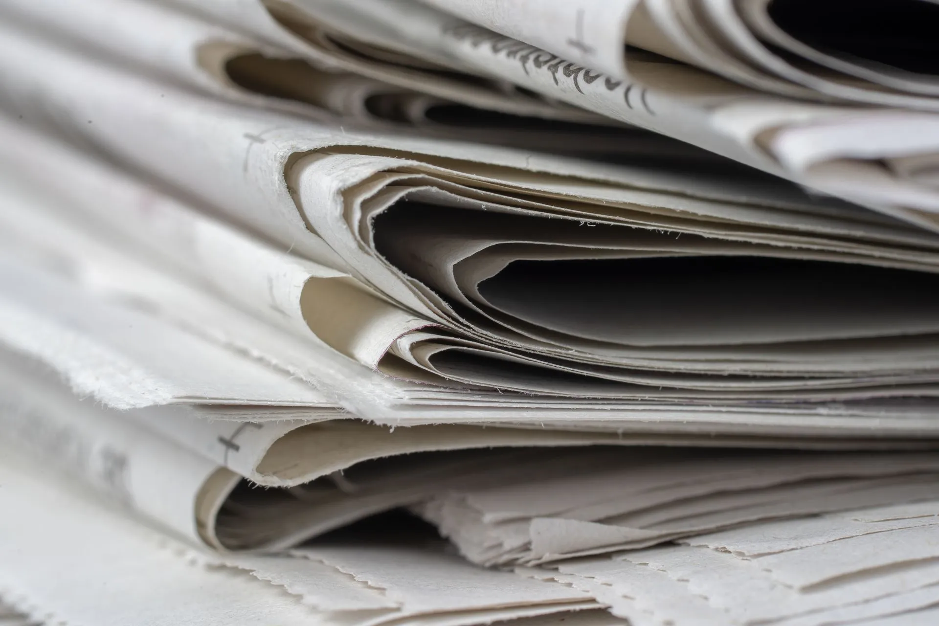 A detailed close-up view of stacked newspapers, highlighting textures and layers, illustrating Cloudflare Pay Per Use and Google's reported publisher pilot put a meter on AI content use