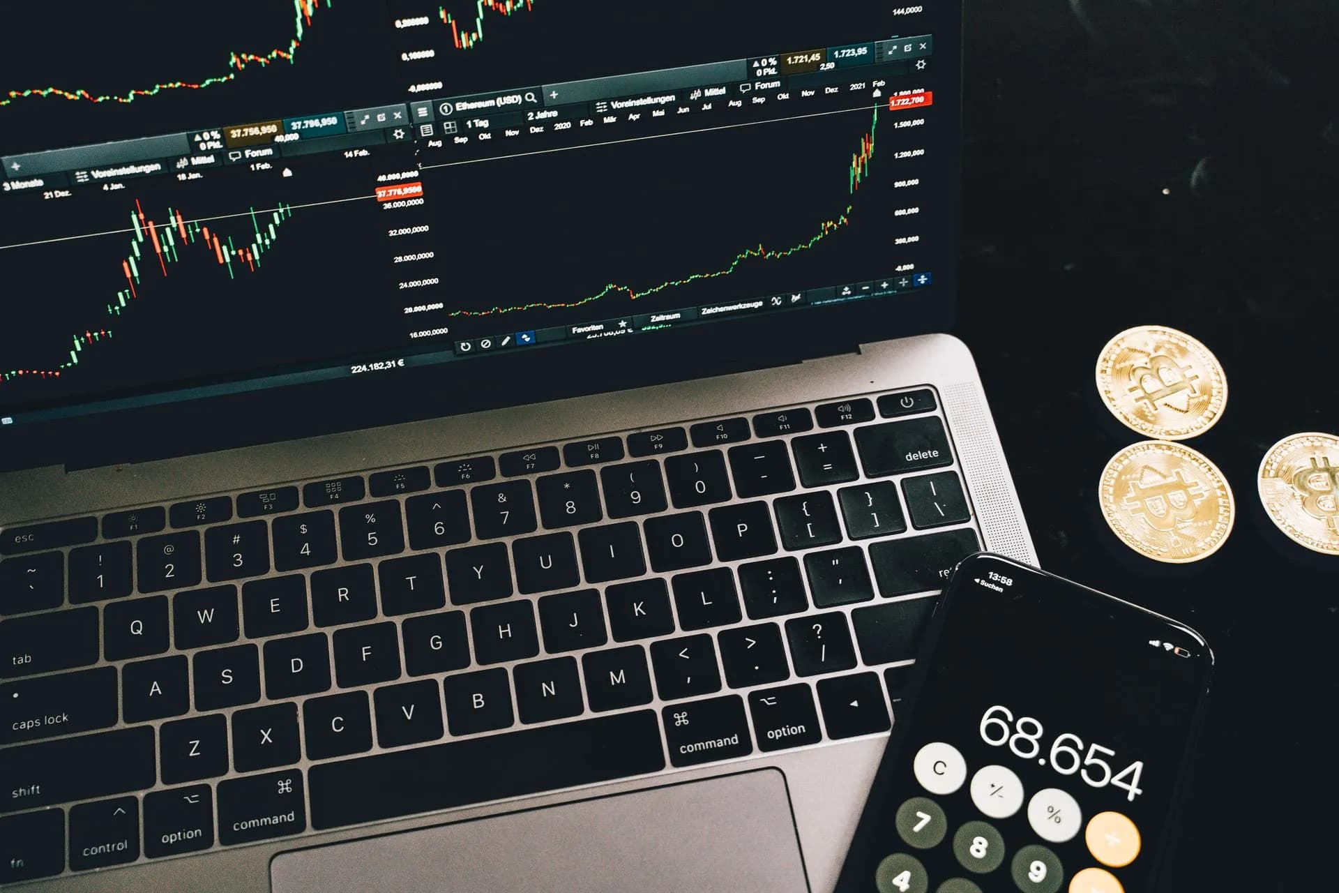 A laptop with trading charts, smartphone calculator, and bitcoin coins depicting cryptocurrency trading, illustrating Deno joins Cloudflare, with Ryan Dahl leading a push for
