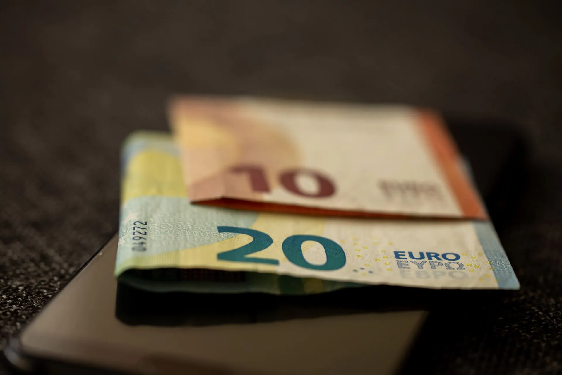 A detailed close-up shot of 10 and 20 euro banknotes placed on a smartphone, representing finance and technology, illustrating ECB invites firms to help shape the digital euro, with
