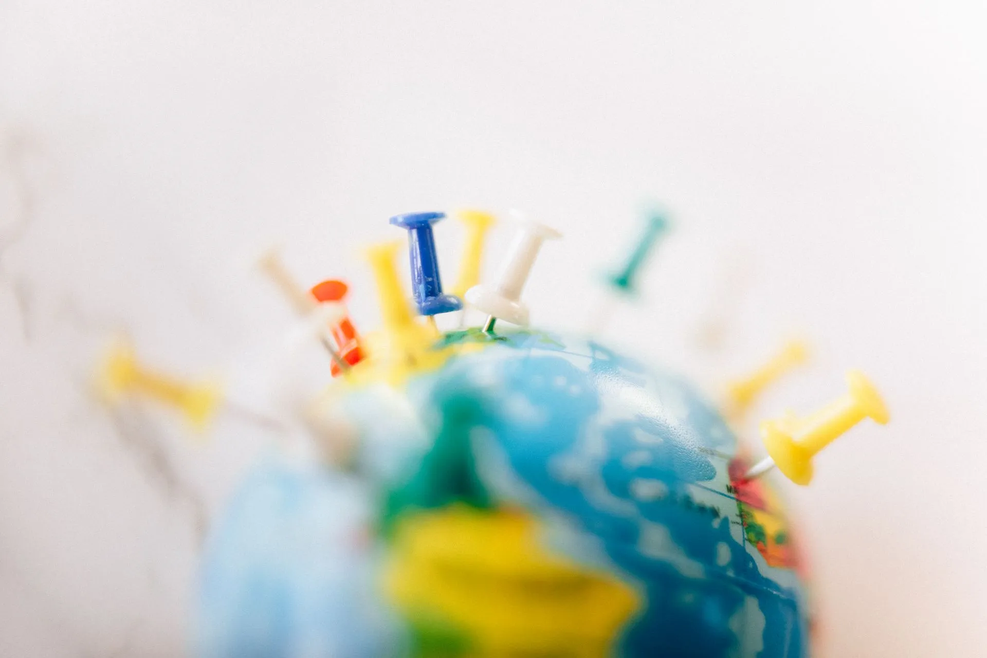 Vibrant close-up of a globe marked with multicolored push pins on a white background, illustrating Endeavor Catalyst closes $320M Fund V to back founders outside major tech hubs