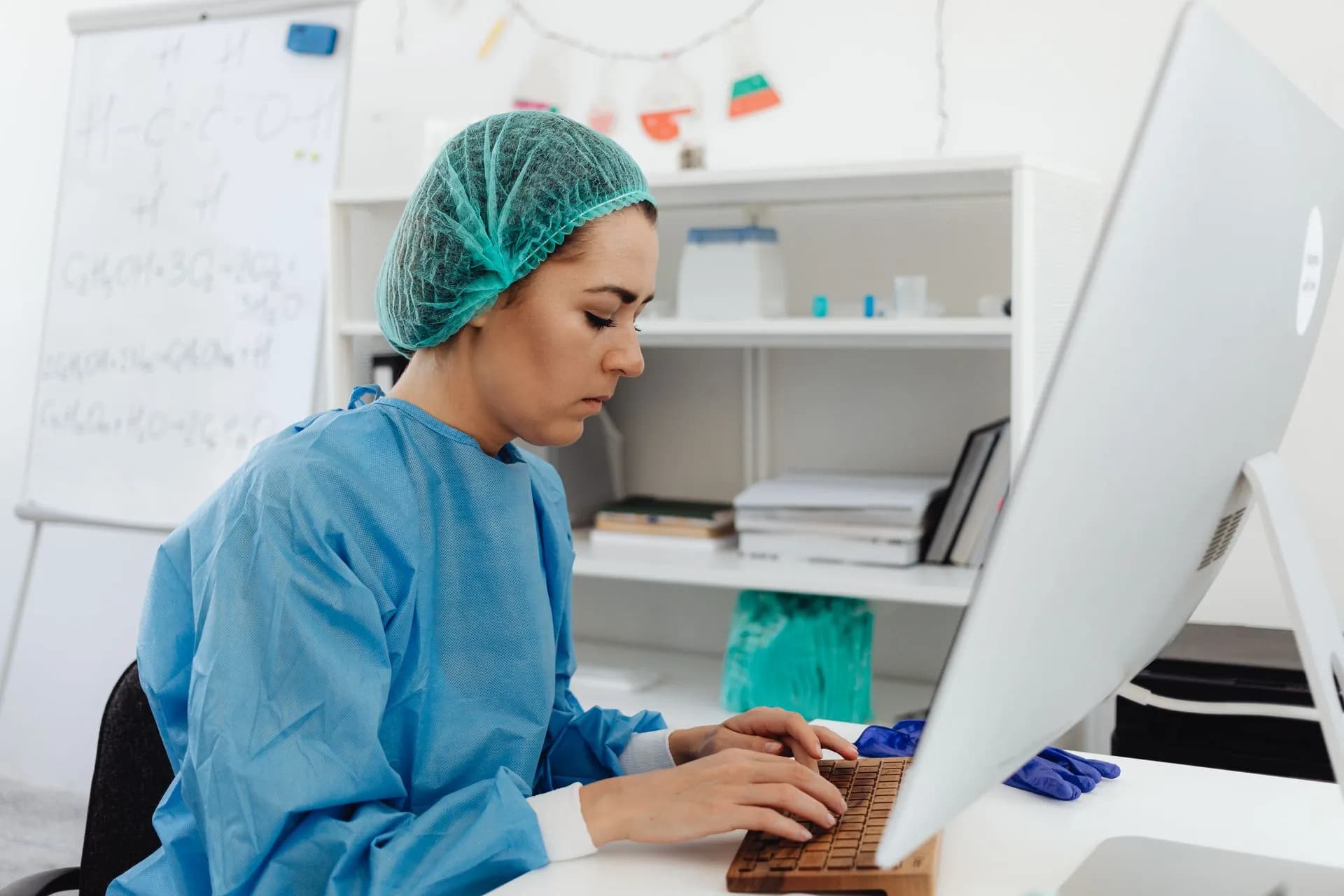 A female healthcare professional in scrub suit working on a computer in a laboratory setting, illustrating Epic pauses most product development to fix MyChart security flaws found with