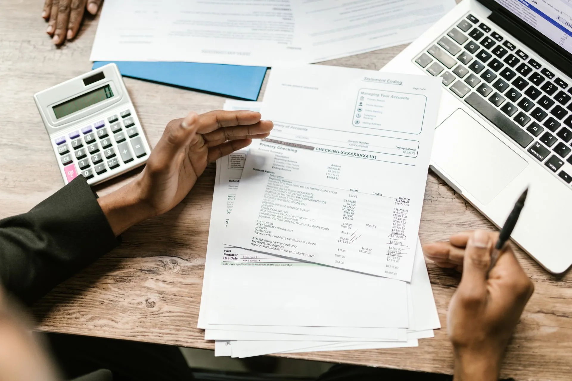 Hands holding financial documents with calculator and laptop on office desk, business analysis scene, illustrating Experian launches Cashflow Data Bureau to put bank-account data into