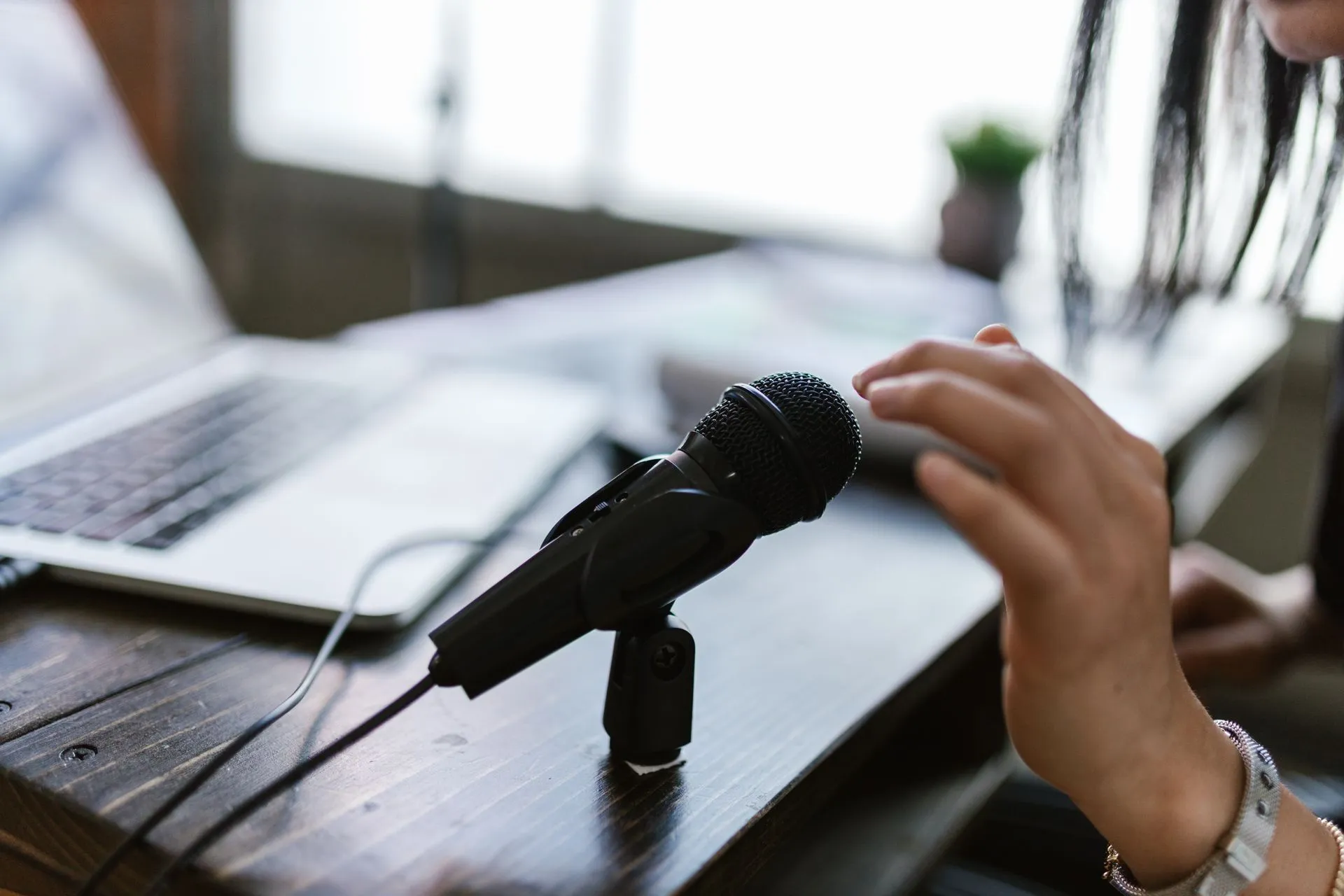 Close-up of a microphone and hand near a laptop, ideal for podcasting themes, illustrating Fireflies Talk makes unlimited voice dictation free, taking aim at Wispr Flow