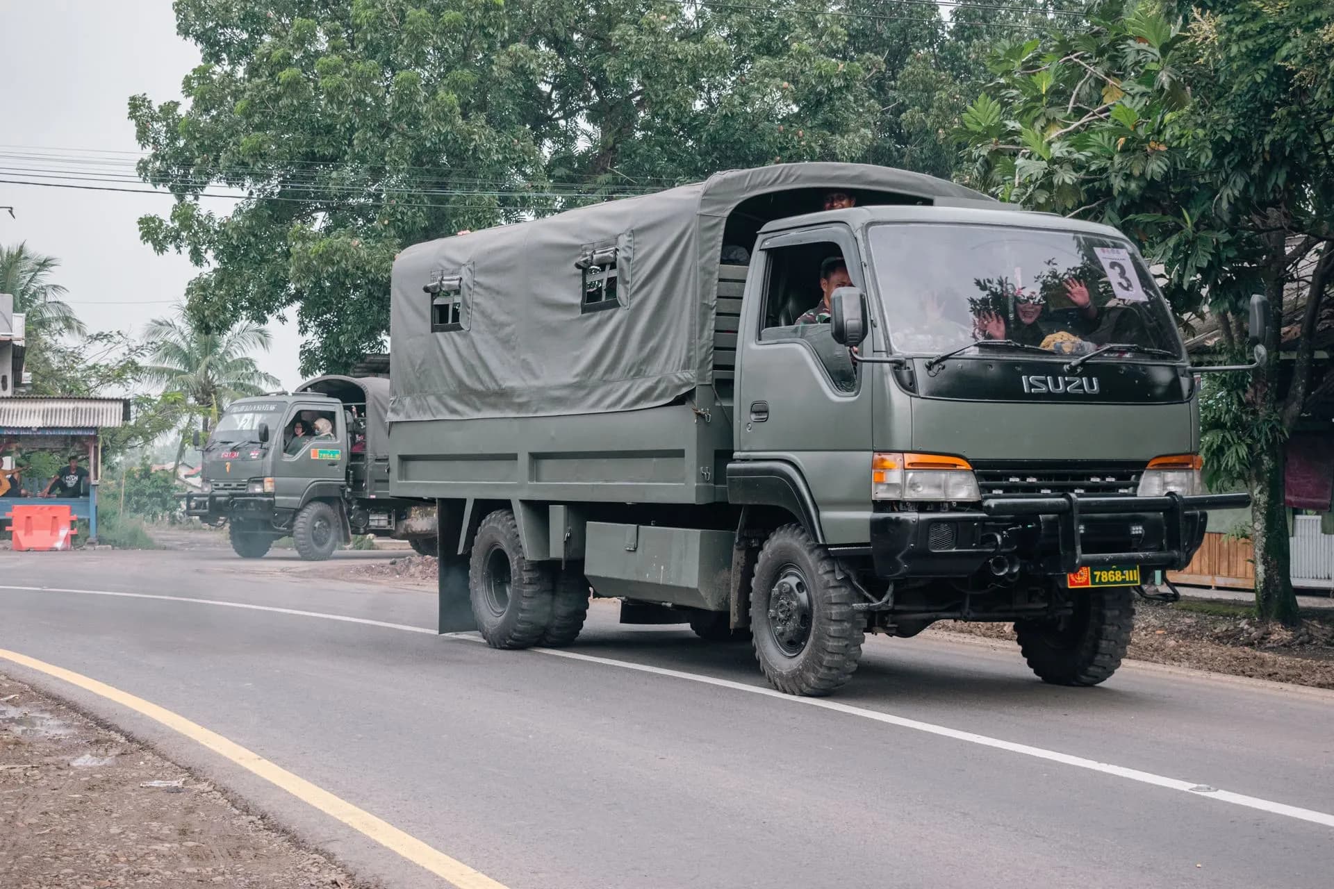 Military trucks traveling on a rural road surrounded by trees and local buildings, illustrating Gallatin AI raises $50M Series A for its Navigator military logistics platform