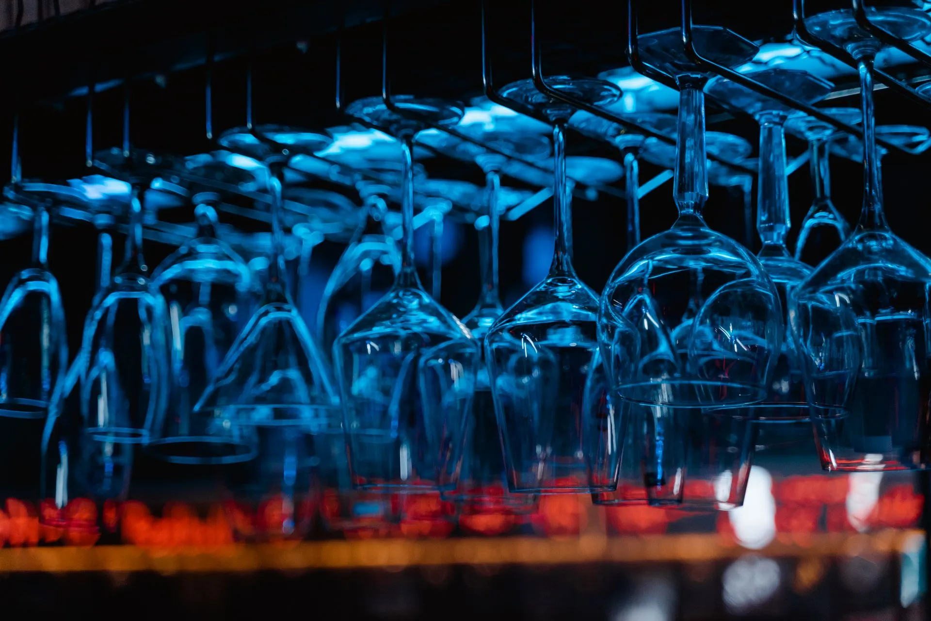 Close-up of glassware hanging upside down inside a bar, illuminated with blue light, illustrating GitHub rebuilds its Git storage as AI agents push commits to 7.38 billion a month