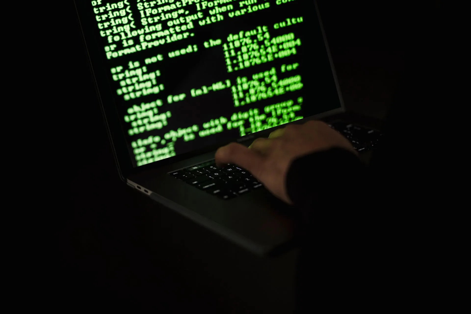 Crop unrecognizable computer geek typing on netbook with codes on screen while hacking system in darkness, illustrating Hadrian raises $40 million Series B for autonomous offensive