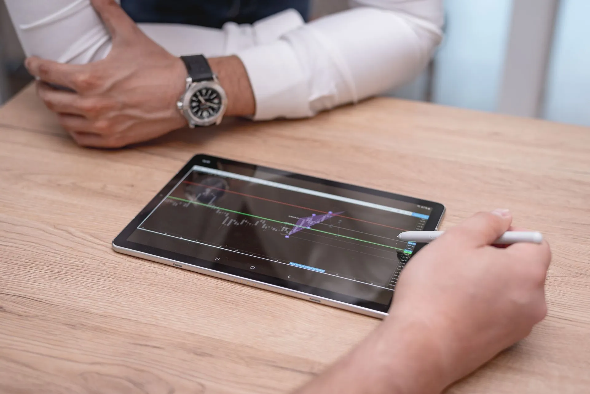 Close-up of hands using a digital tablet with trading charts on a wooden desk, illustrating IPO window stays narrow outside mega-deals as preliminary Q3 tally shows $34.9 billion