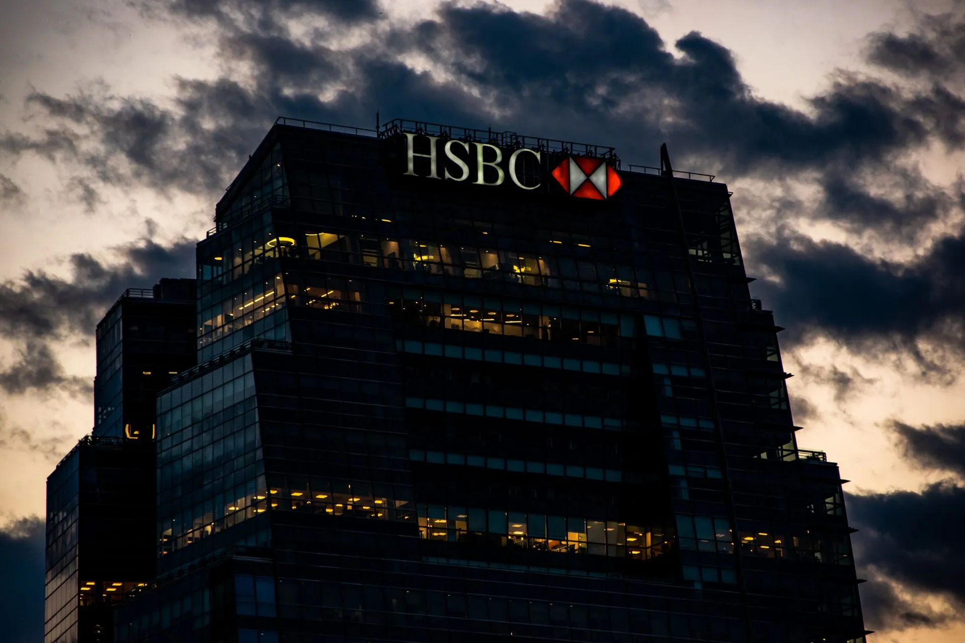Night view of an illuminated HSBC office building against a dramatic evening sky, illustrating JPMorgan HR chief role goes to Mark O'Donovan as Robin Leopold retires in January