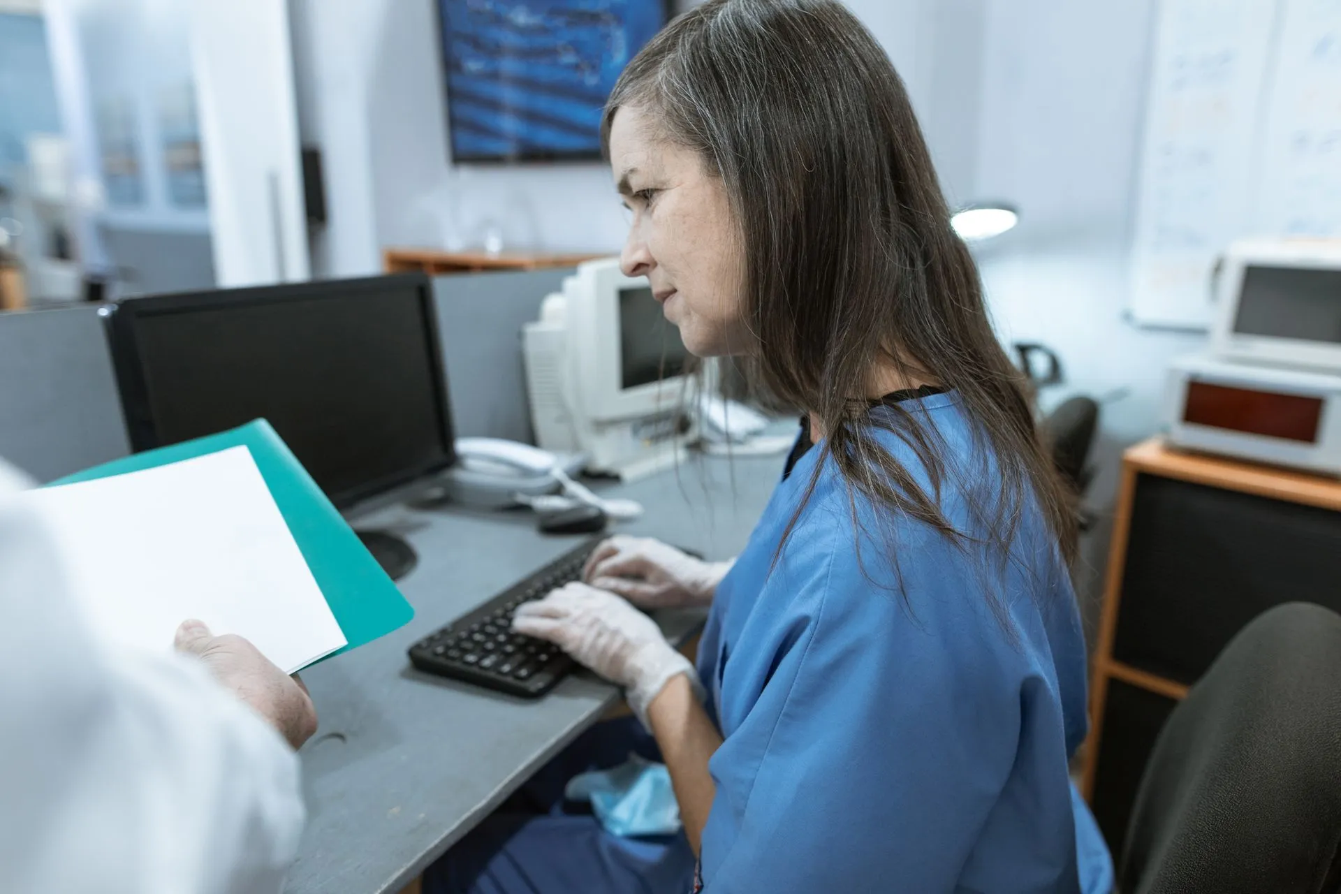 Nurse in scrubs typing on a keyboard at a medical workstation, illustrating Medyc data breach exposes Polish patient data as regulator orders Qbusoft audit