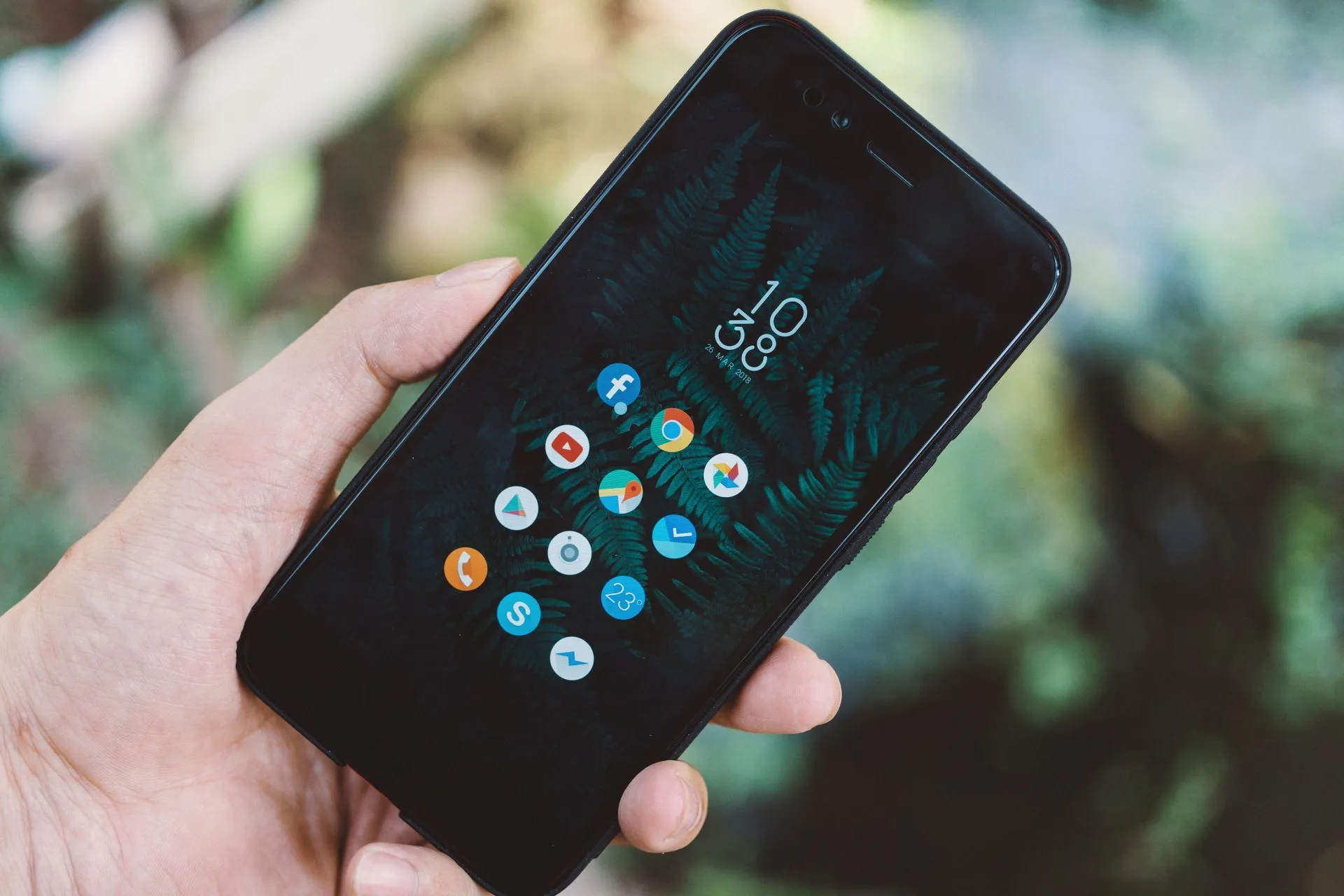 Close-up of a hand holding a smartphone with app icons and a nature wallpaper, illustrating Meta AI advertising tools let marketers plan campaigns by chat and check out in Messenger
