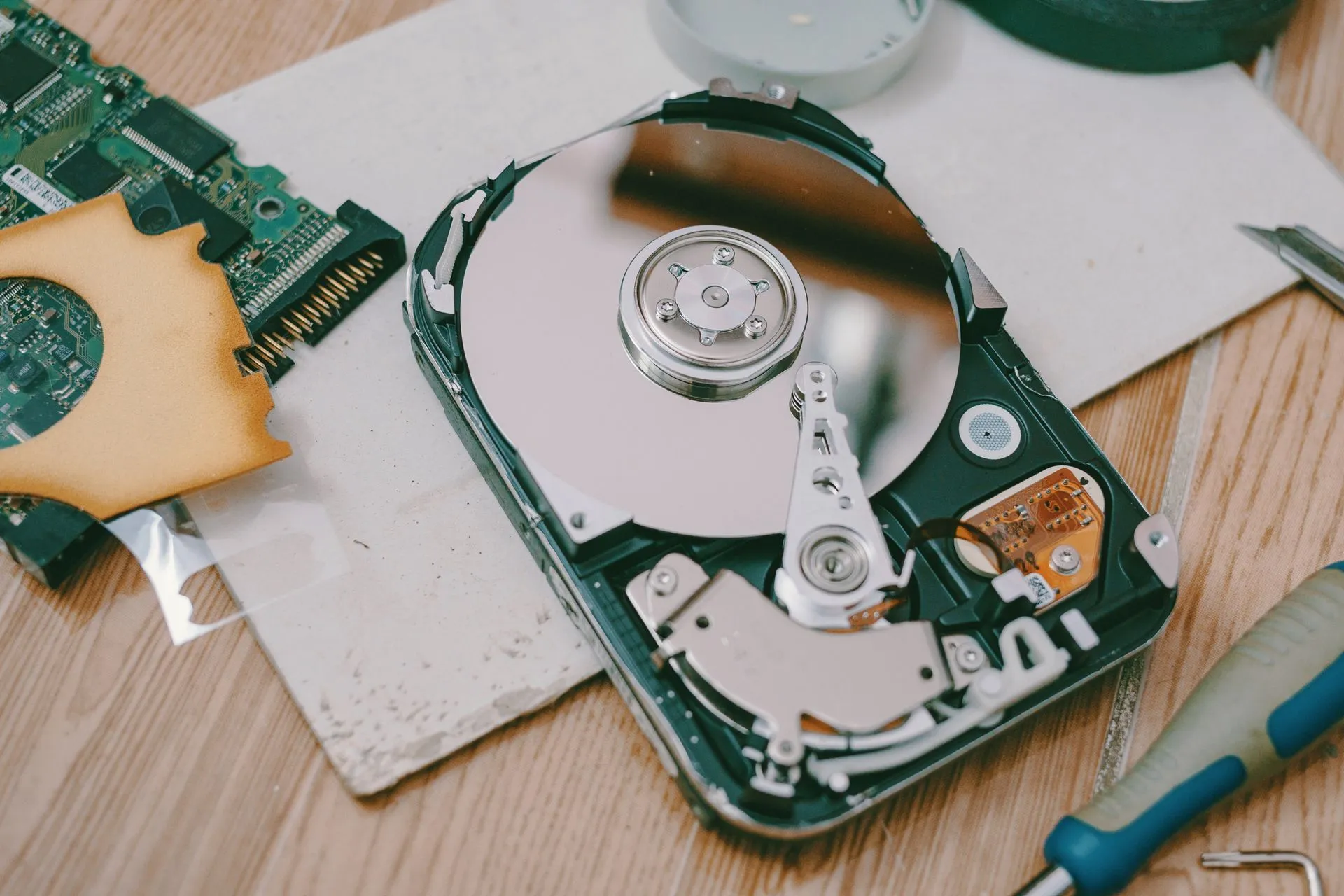 Close-up of a disassembled hard drive showing internal components on a wooden table, illustrating Microsoft says error may have wiped some nonprofits' Microsoft 365 data early, with no