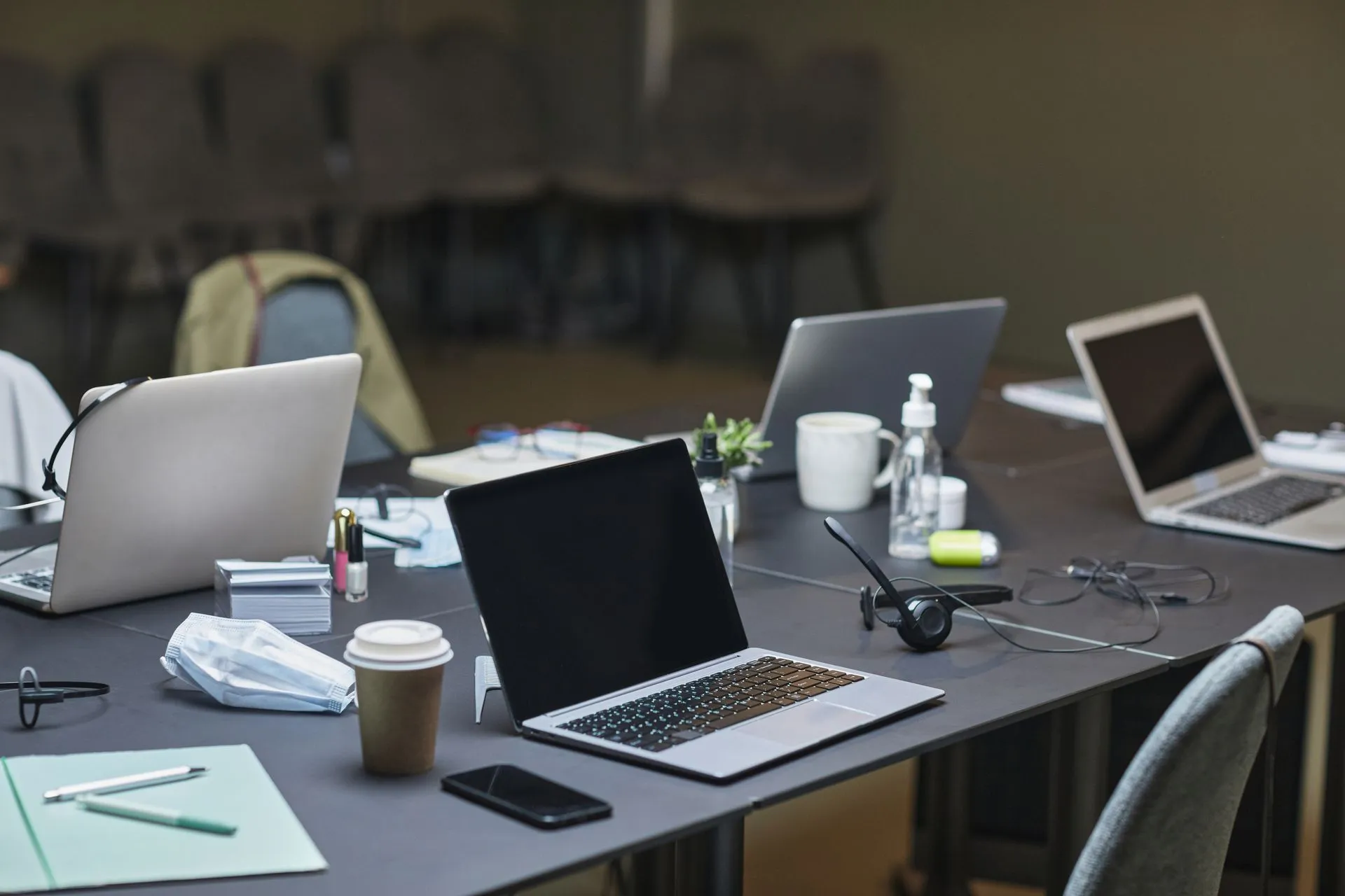 A cluttered office desk setup featuring multiple laptops, coffee cup, and office supplies for a busy workday, illustrating Microsoft deadlines hit IT budgets as Windows 10 support