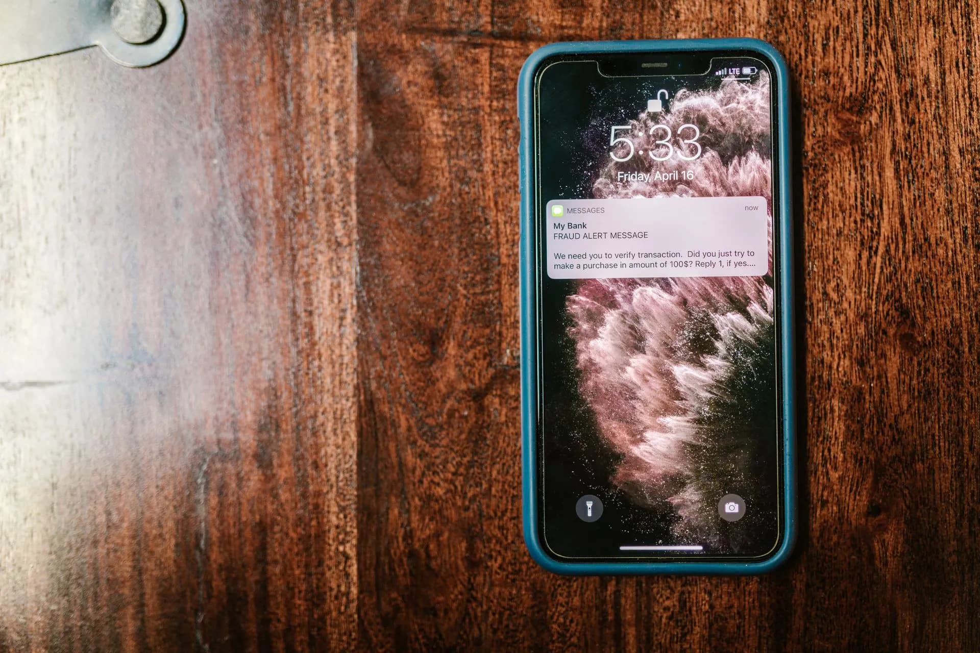 Close-up of a smartphone displaying a fraud alert message on a wooden table, illustrating Midnight Mimosa malware ships preinstalled on budget Android phones in 150+ countries