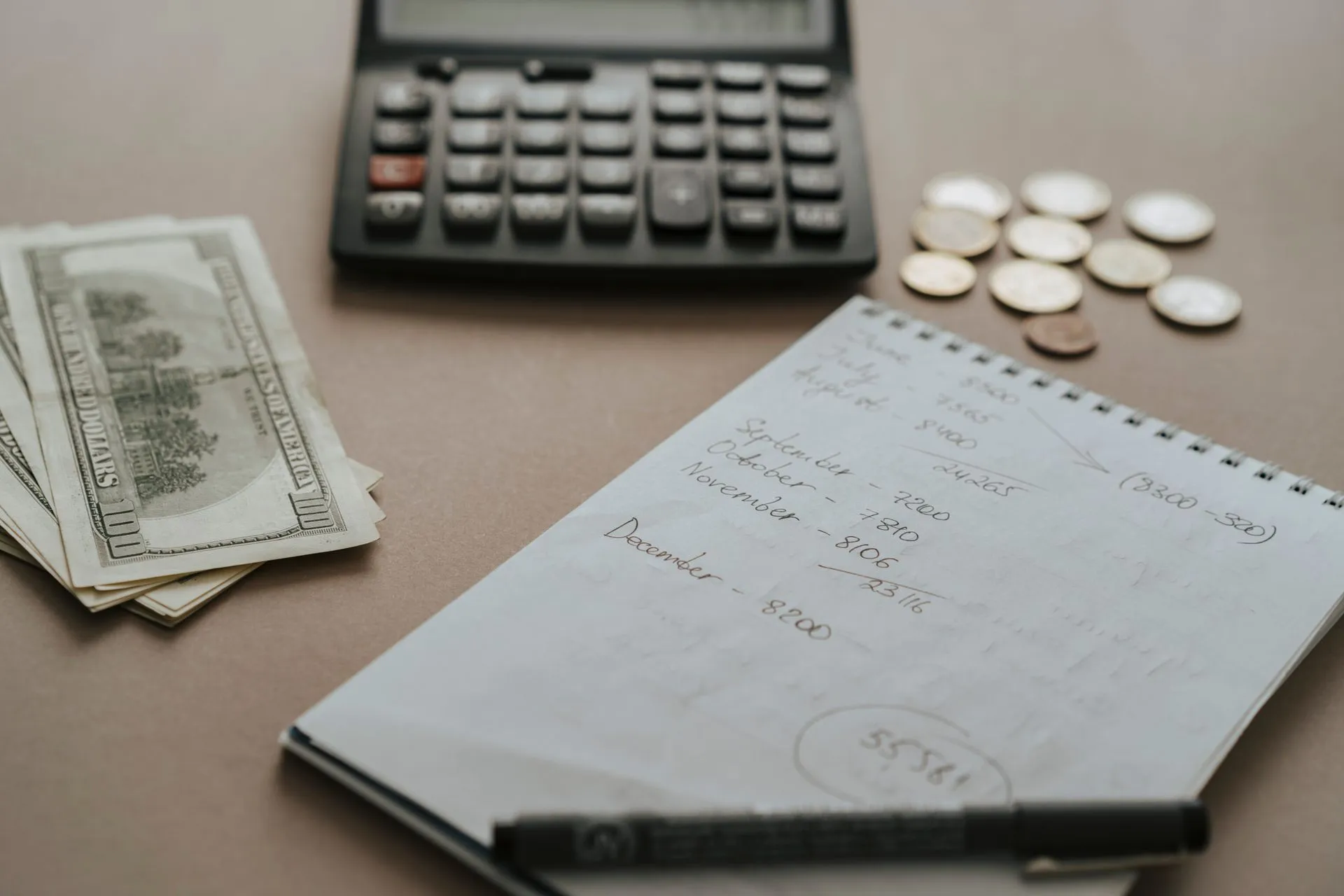 Desk setup showing calculator, cash, coins, and financial notes for budgeting, illustrating Monarch acquires MBI, formerly HMBradley, as the budgeting app hits $100 million in ARR