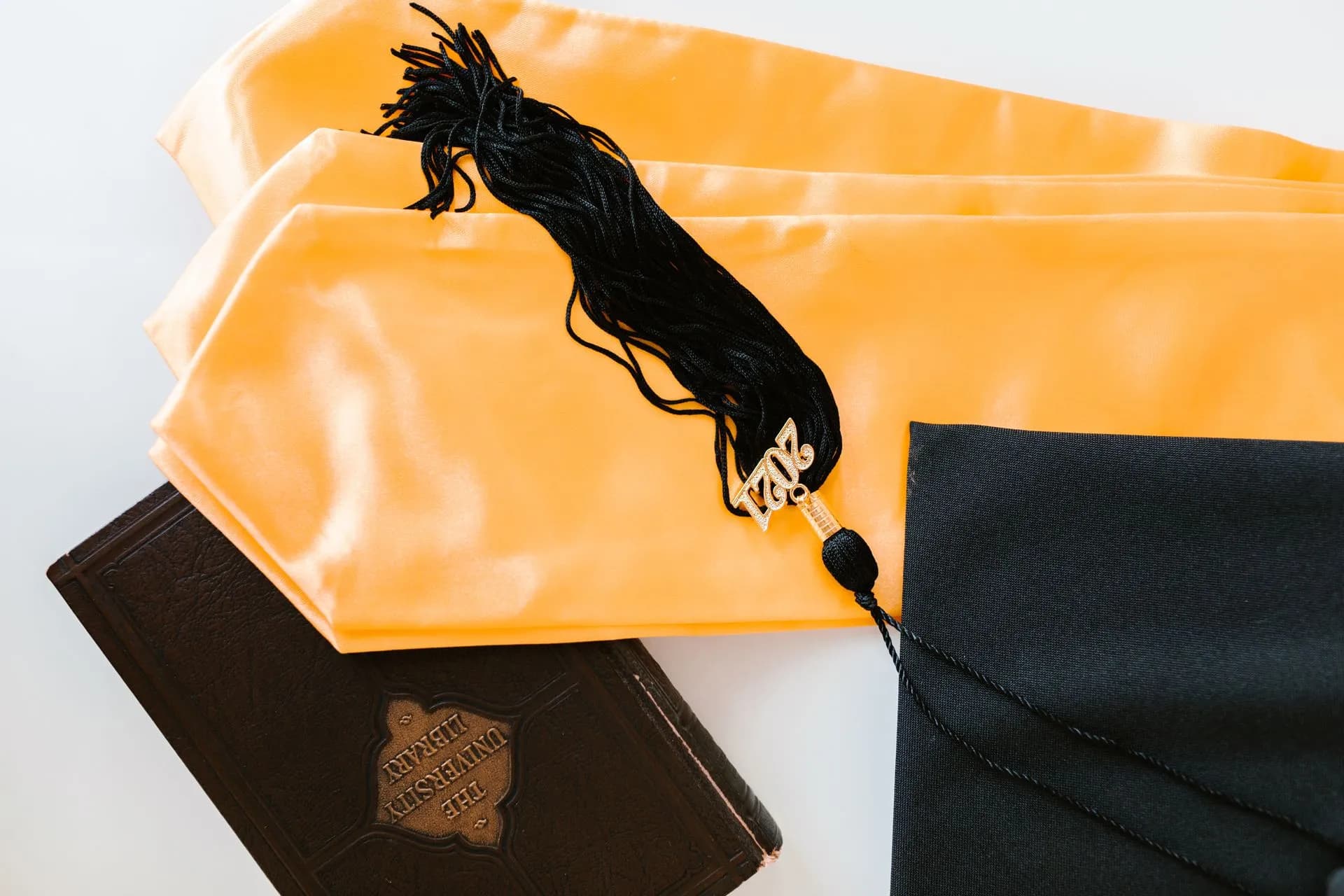 Close-up of graduation cap, gown, and tassel with year charm and a book, illustrating Student lender Mpower shuts down after Zimbabwe travel ban hits demand for its loan-backed bonds