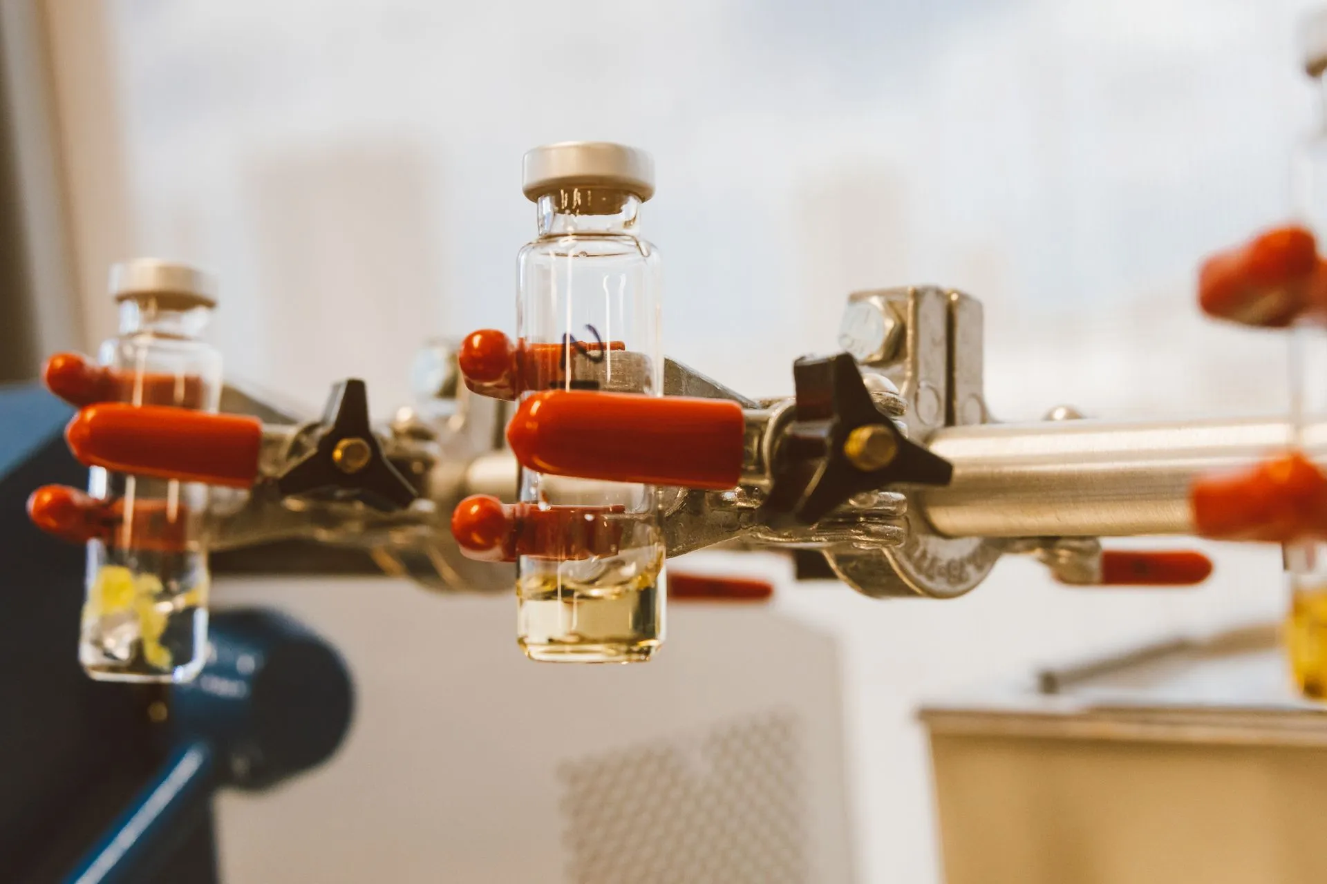 Detailed view of laboratory glass vials held by a clamp with red handles, ideal for science stock images, illustrating Multiply Labs raises $75 million for robots that make cell and