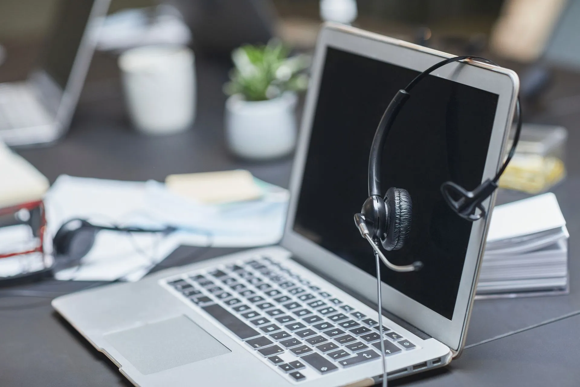 A headset placed on a laptop in a modern, cluttered office setting with papers and plants, illustrating Omnissa AI agents target IT work as company says three-quarters of AI use is