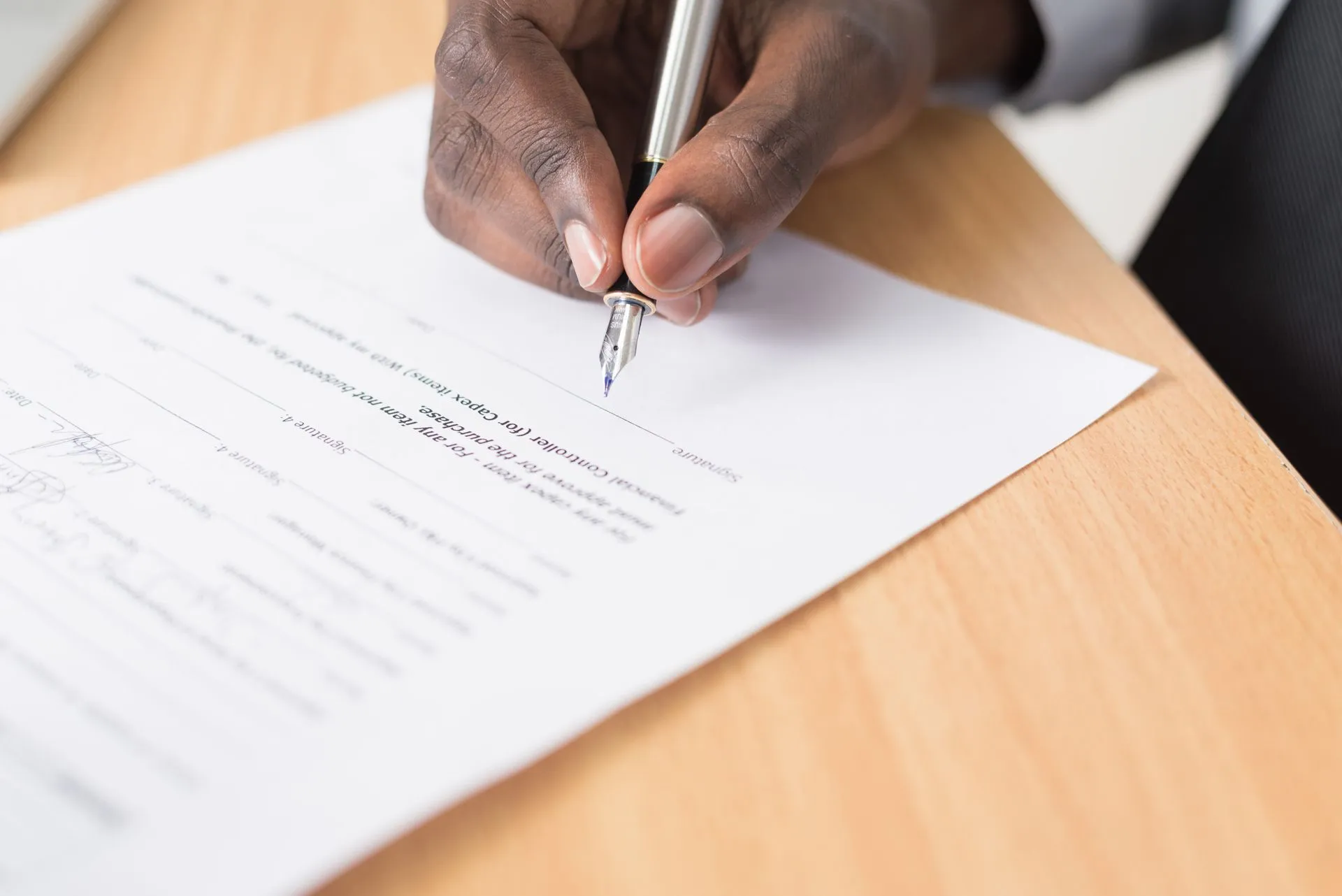 A hand holding a pen signing a document close-up on a desk, symbolizing agreement or contract finalization, illustrating OpenAI's Medicare breach apology and safety-case proposal raise