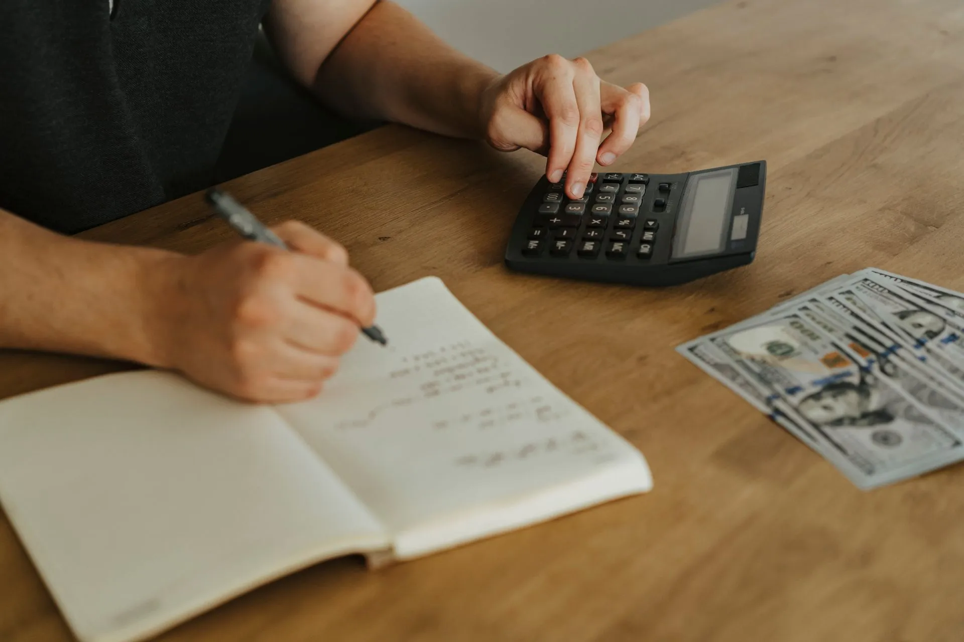 Close-up of hands using a calculator with notebook and cash on a wooden table, illustrating Oracle Fusion Claw adds 25 AI agent apps that reconcile accounts and redo staffing plans