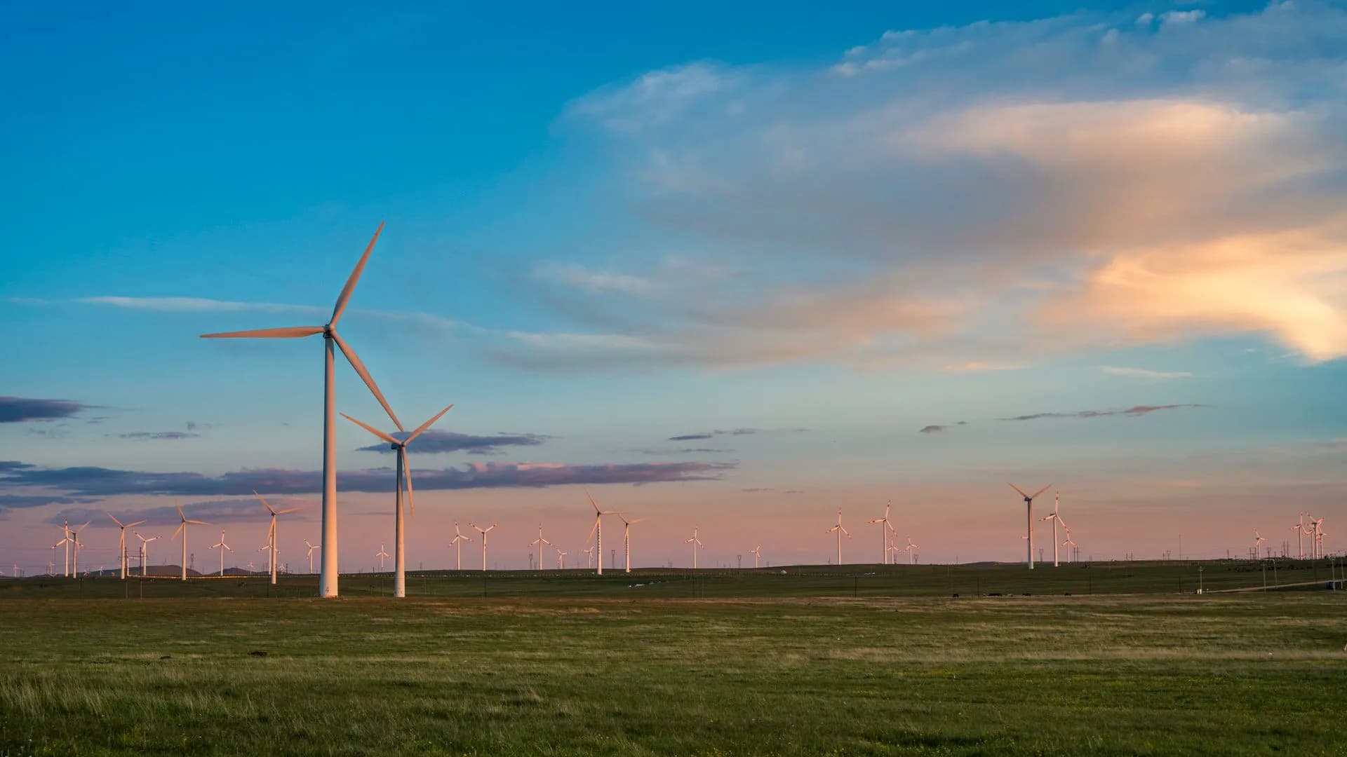 View of a wind farm with multiple turbines under a colorful dusk sky. Renewable energy source.