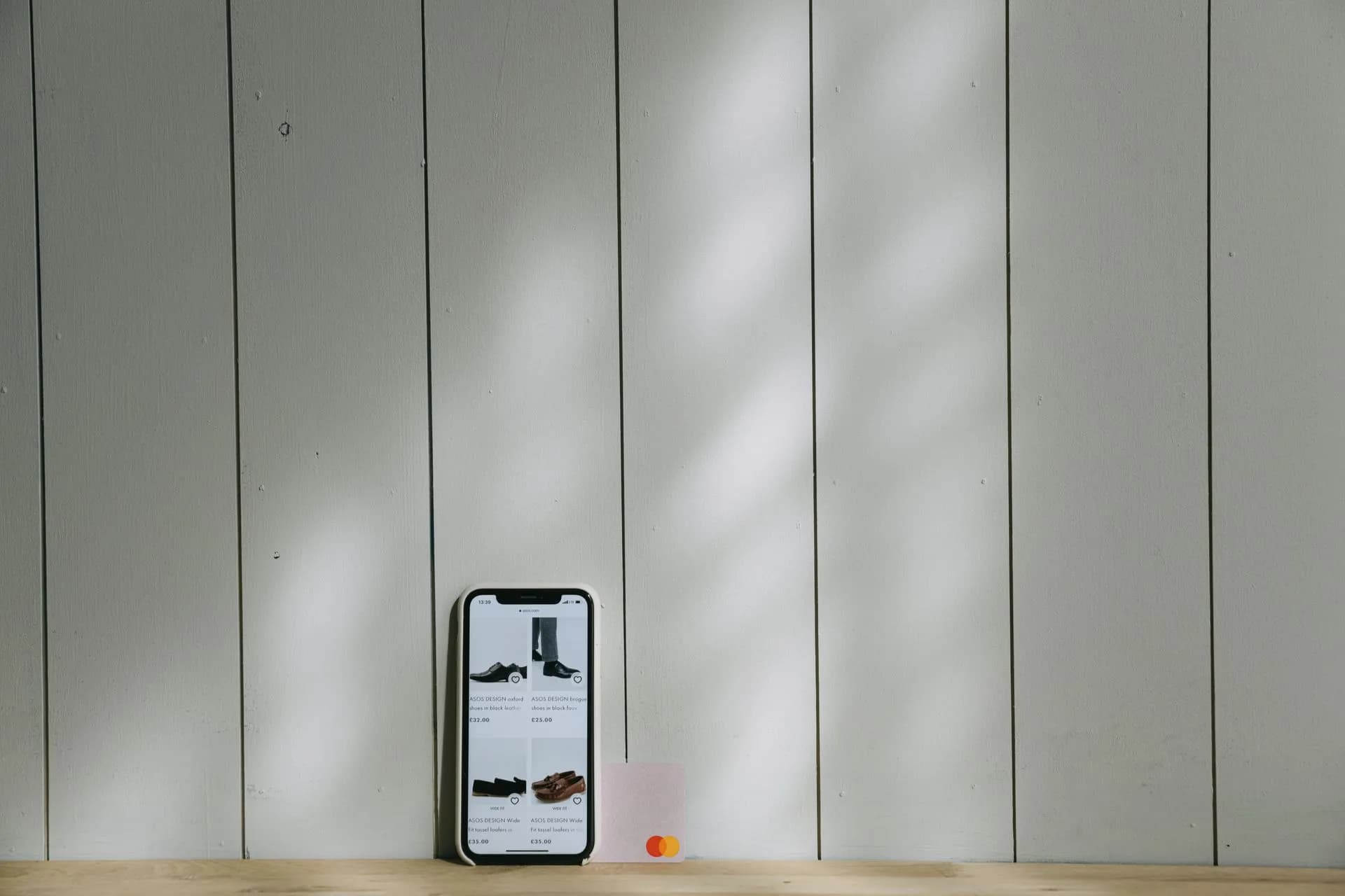 A smartphone and credit card sit on a wooden surface with soft lighting shadows.