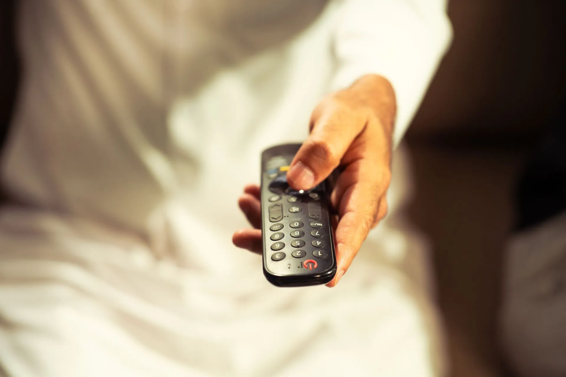 Close-up of a hand holding a TV remote control, representing relaxation at home, illustrating Ynon Kreiz leaves Mattel to be co-CEO with David Ellison as Paramount closes WBD deal