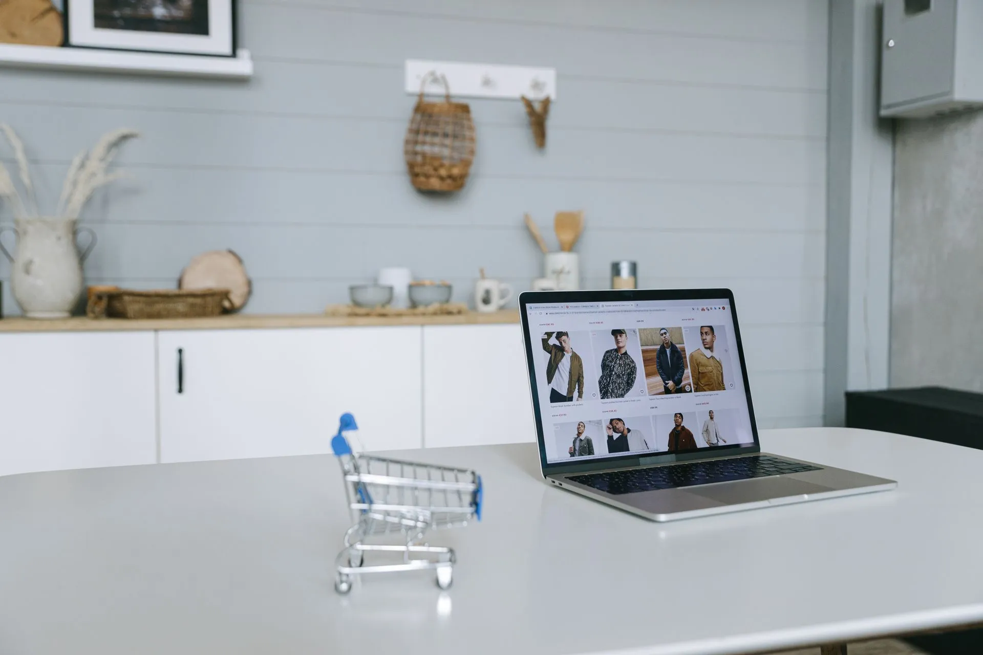 A laptop displaying an online shopping portal sits on a minimal desk with a miniature shopping cart in focus, illustrating Meta and Sierra launch Personal Agent Protocol as Amazon and