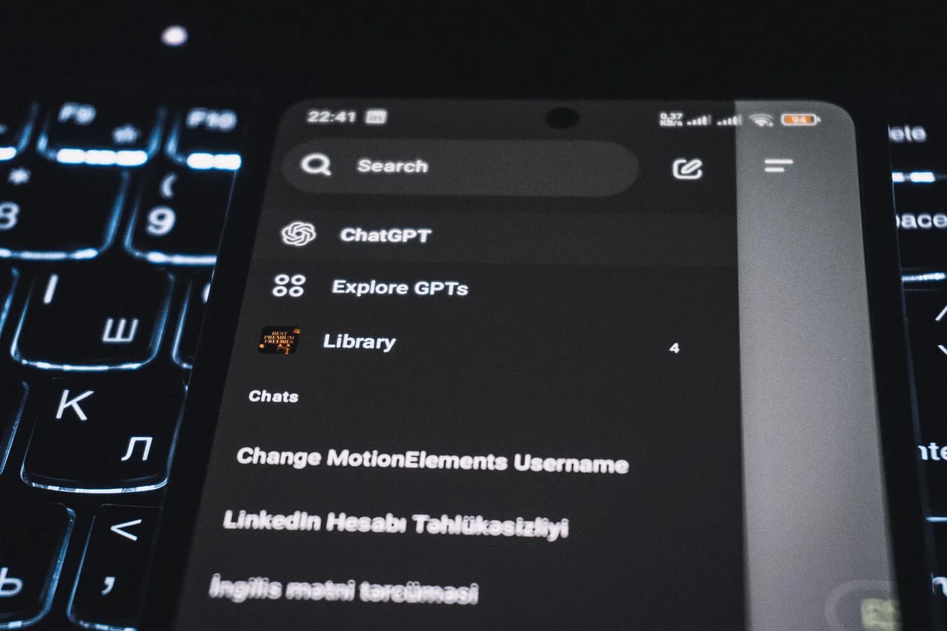Close-up of a smartphone displaying a chat app interface with a backlit keyboard in the background, illustrating Tab debuts at a $300M valuation as Underdog and Hark pitch privacy in