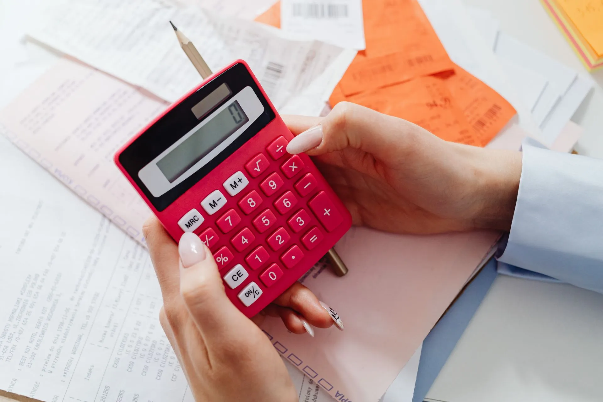 Close-up of hands holding a red calculator, managing finances with documents and receipts, illustrating Personio acquires Circula, adding spend management for 3,000+ firms to its HR