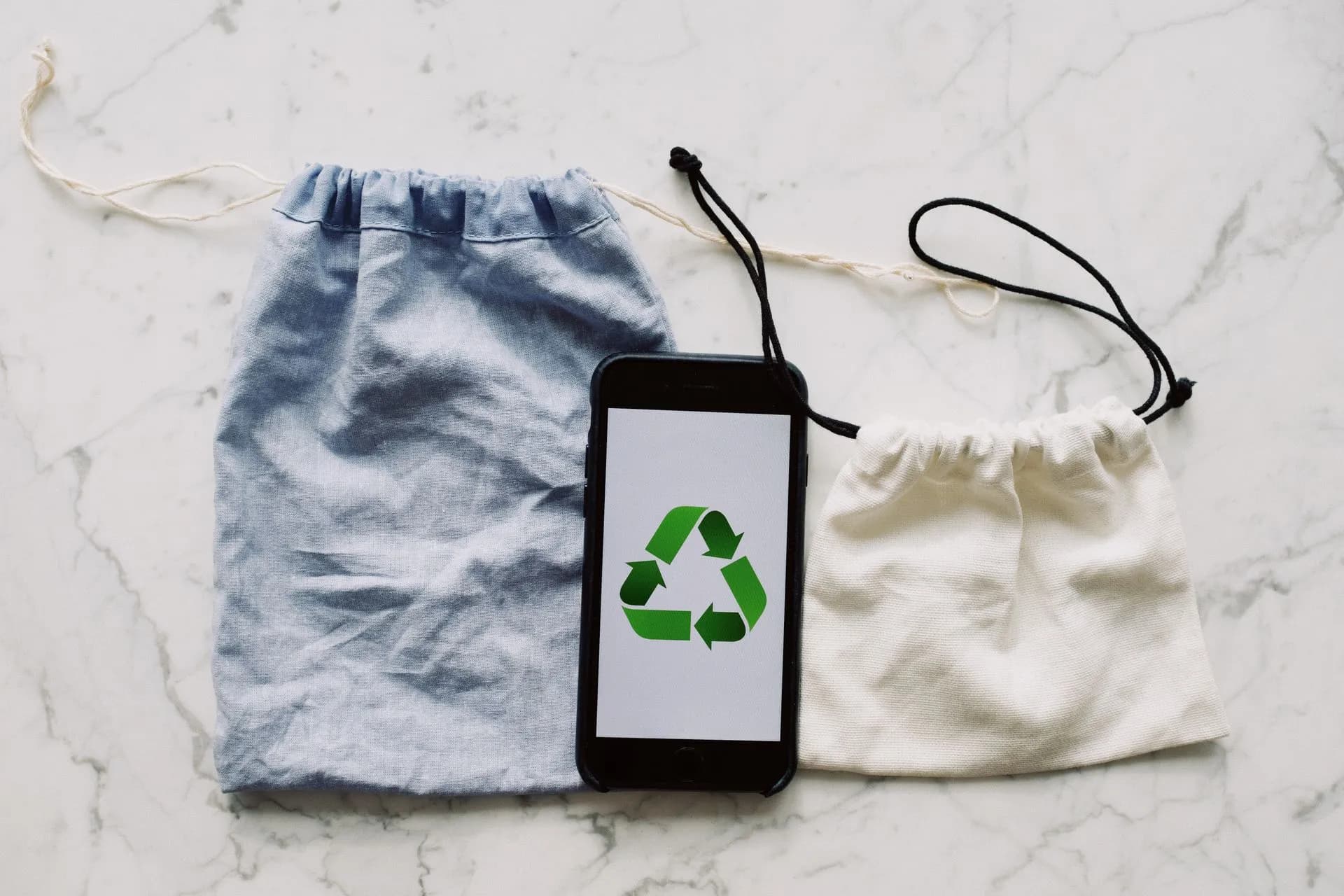 From above view of smartphone with recycling symbol on screen placed between white and blue textile bag on marble table, illustrating Met Police pauses Oxygen phone forensics over alleged